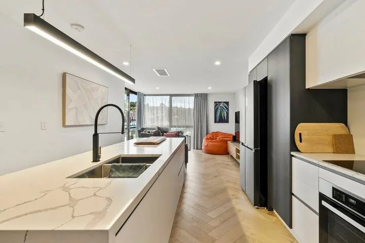 A modern kitchen opens onto a living area, with a long island and dark cabinetry.