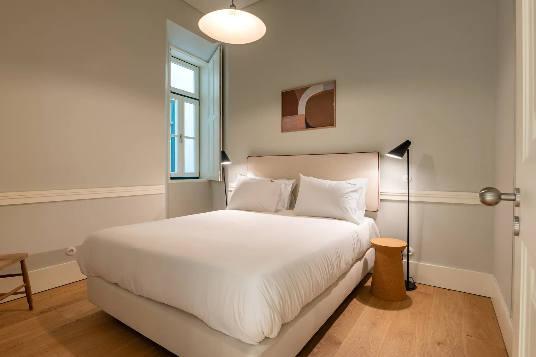 Dormitorio con una cama hecha, lámparas de noche y una ventana.