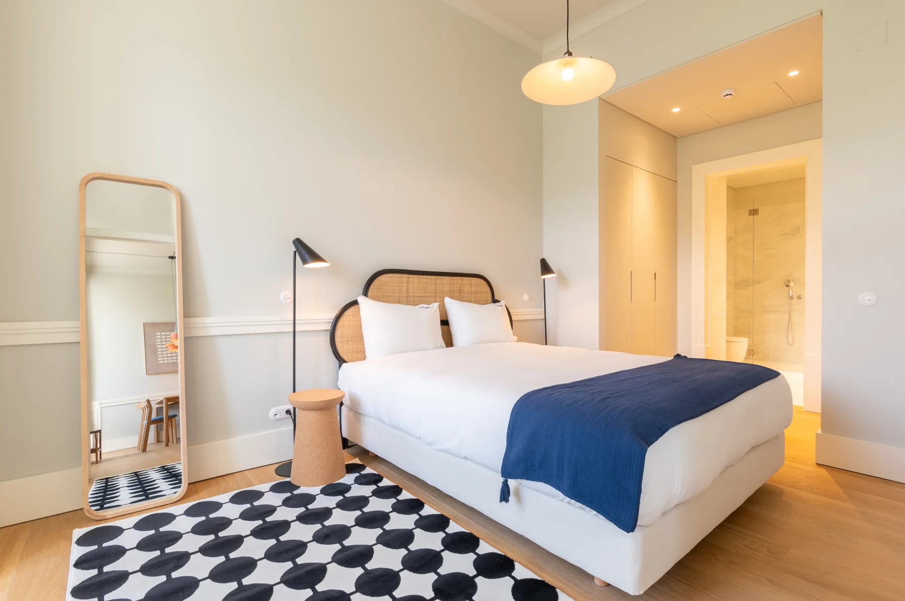 Un dormitorio luminoso con una cama, una alfombra estampada y un espejo de cuerpo entero.