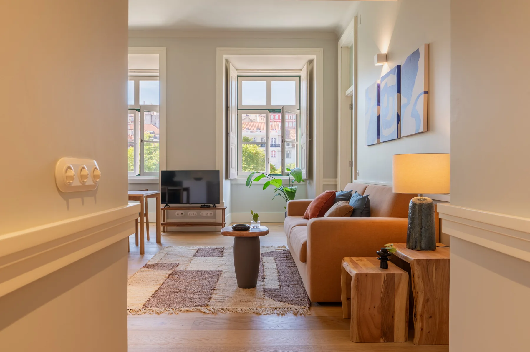 Una sala de estar luminosa con asientos, un televisor y ventanas altas.