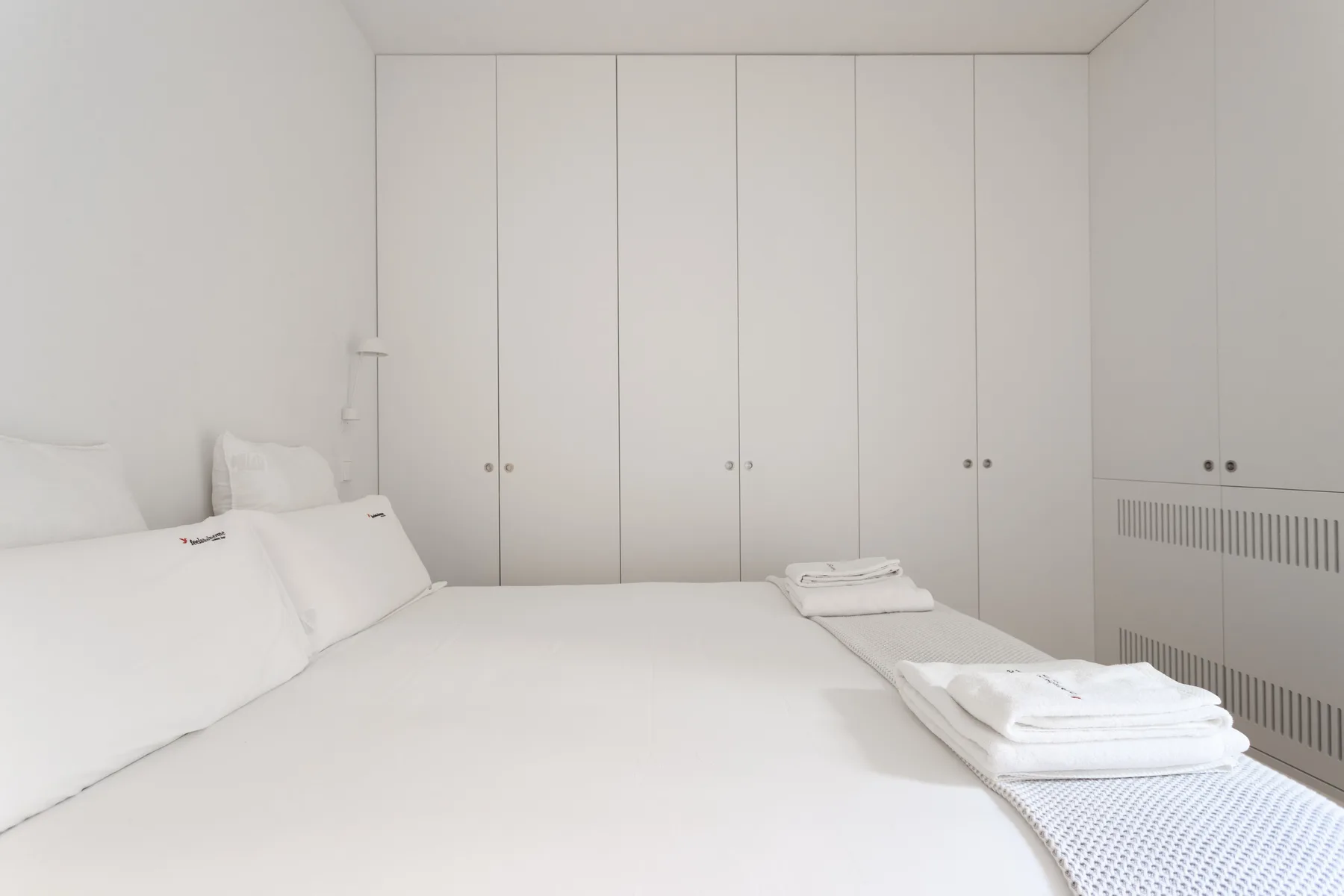 Un dormitorio luminoso con ropa de cama blanca y armarios empotrados.