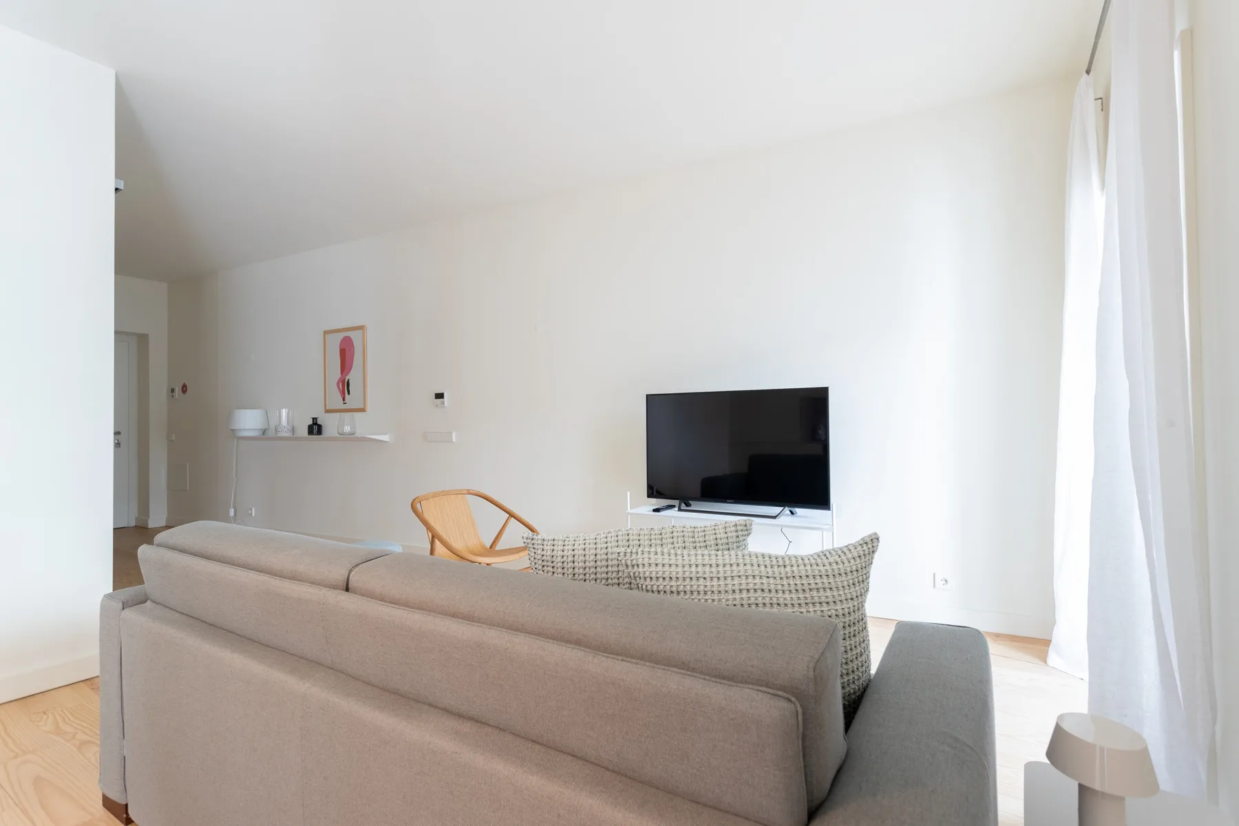 Una sala luminosa con asientos, un televisor y una ventana grande.