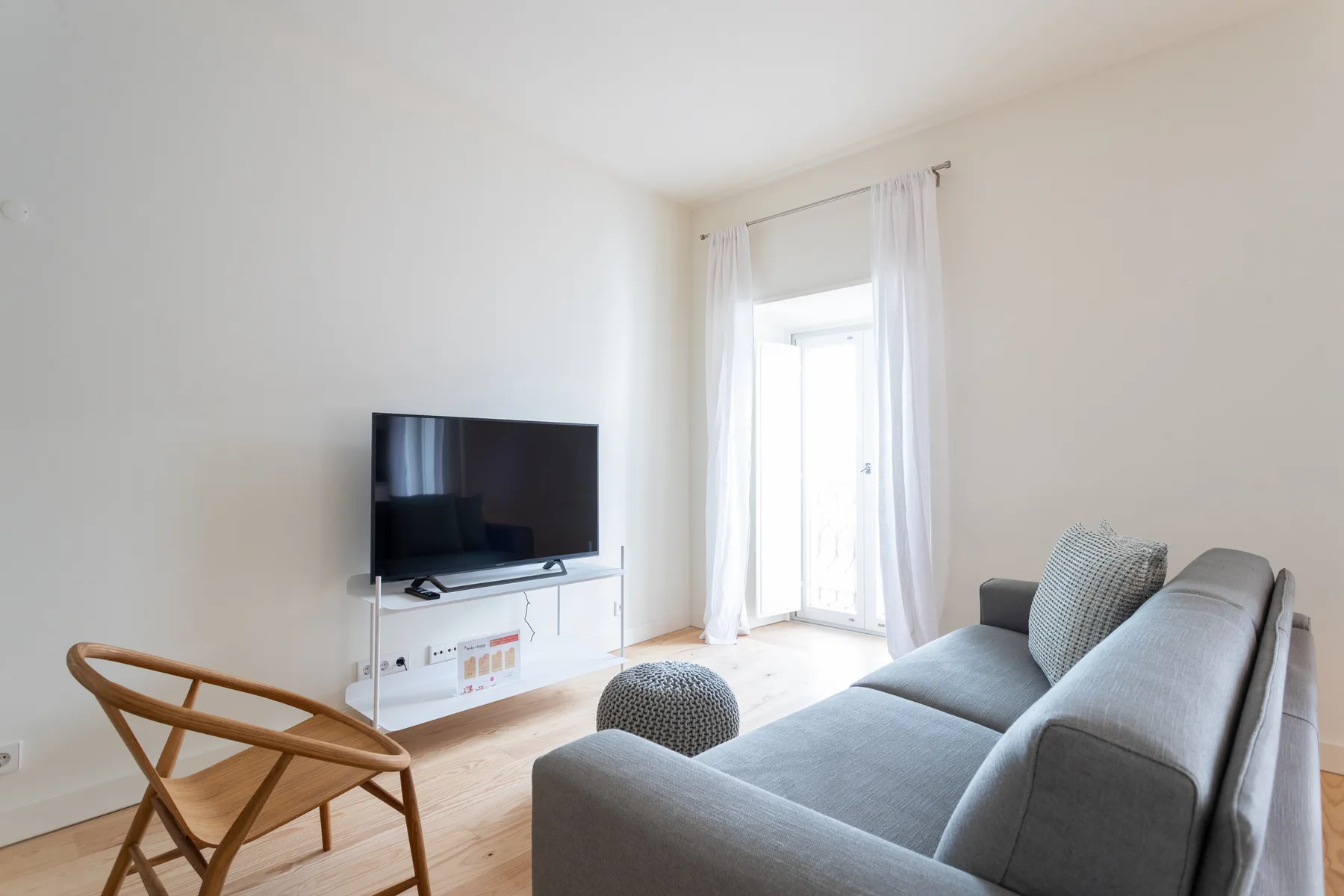 Una sala de estar luminosa con asientos, un televisor y una puerta de vidrio.