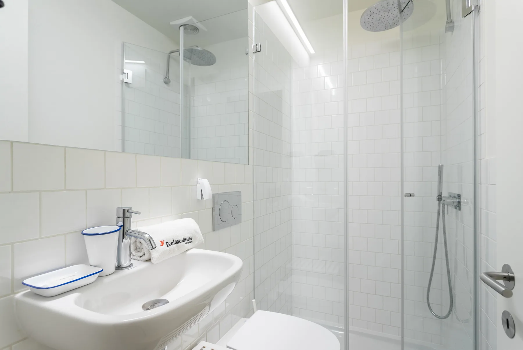 Un baño luminoso con azulejos, lavabo y ducha con mampara de vidrio.
