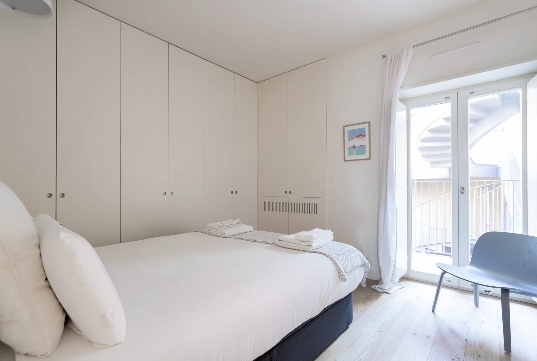 Un dormitorio luminoso con una cama tendida, armarios empotrados y una puerta de cristal al balcón.