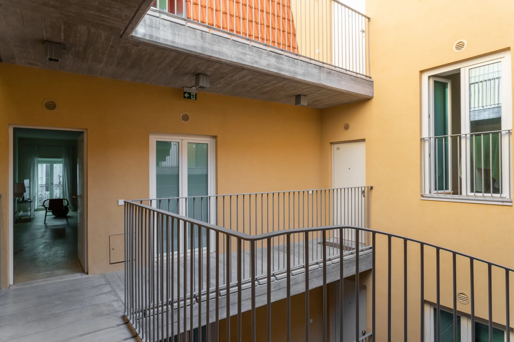 Un pasillo con balcones interiores, barandillas metálicas y puertas.