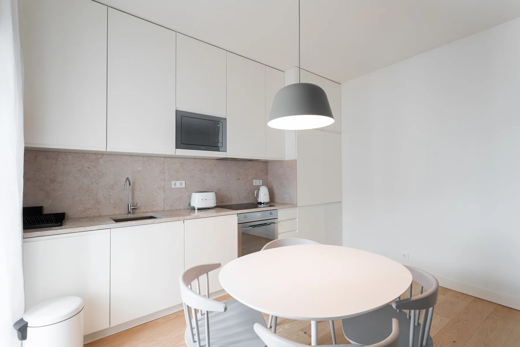 Una cocina moderna y zona de comedor con armarios blancos y una mesa redonda.