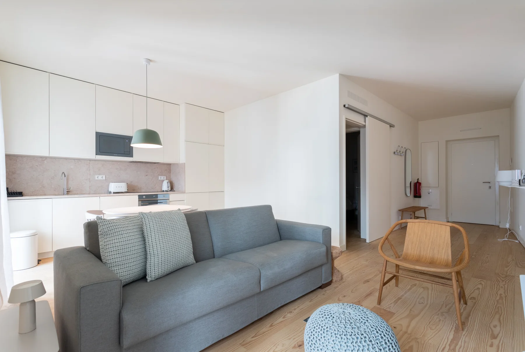 Una zona de estar con asientos grises y una cocina compacta detrás.