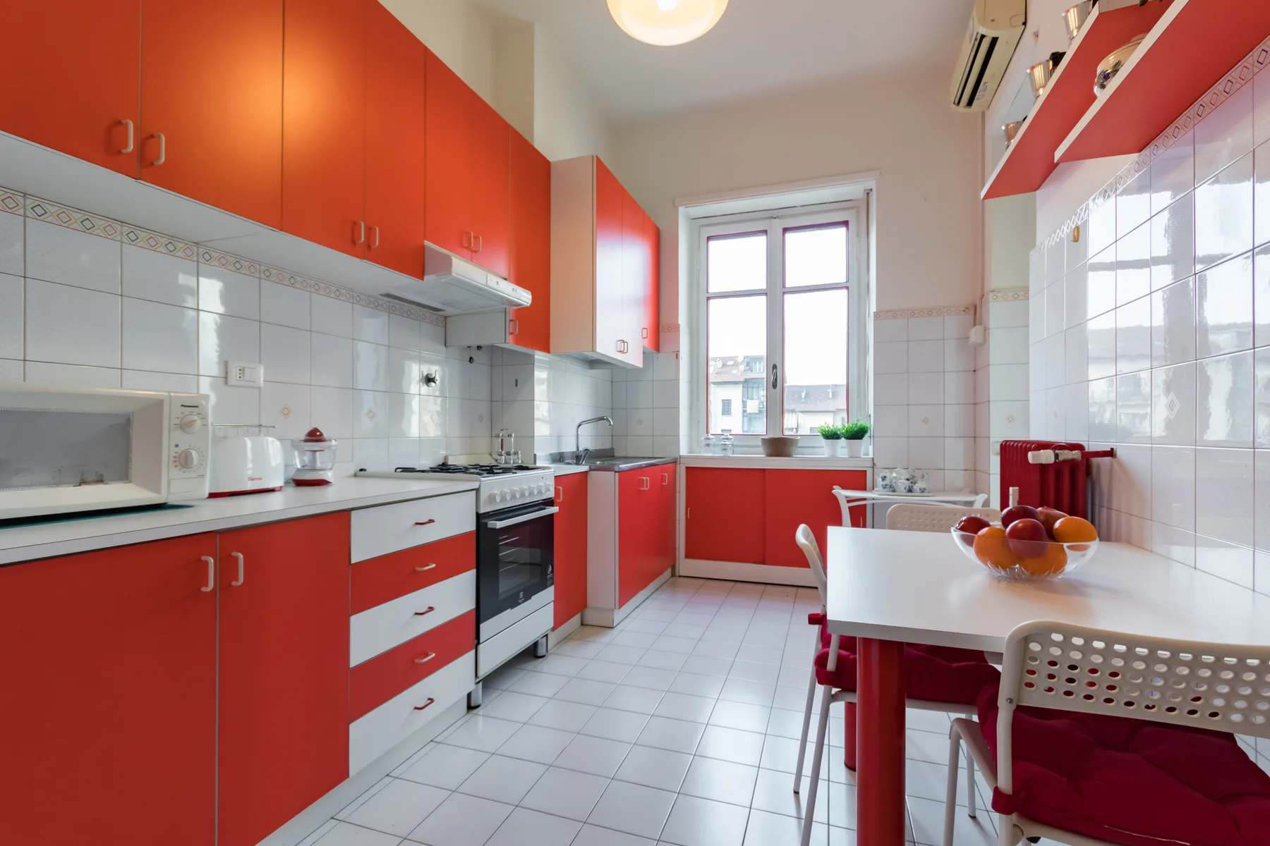 Una cocina luminosa con armarios rojos y una mesa junto a la ventana.