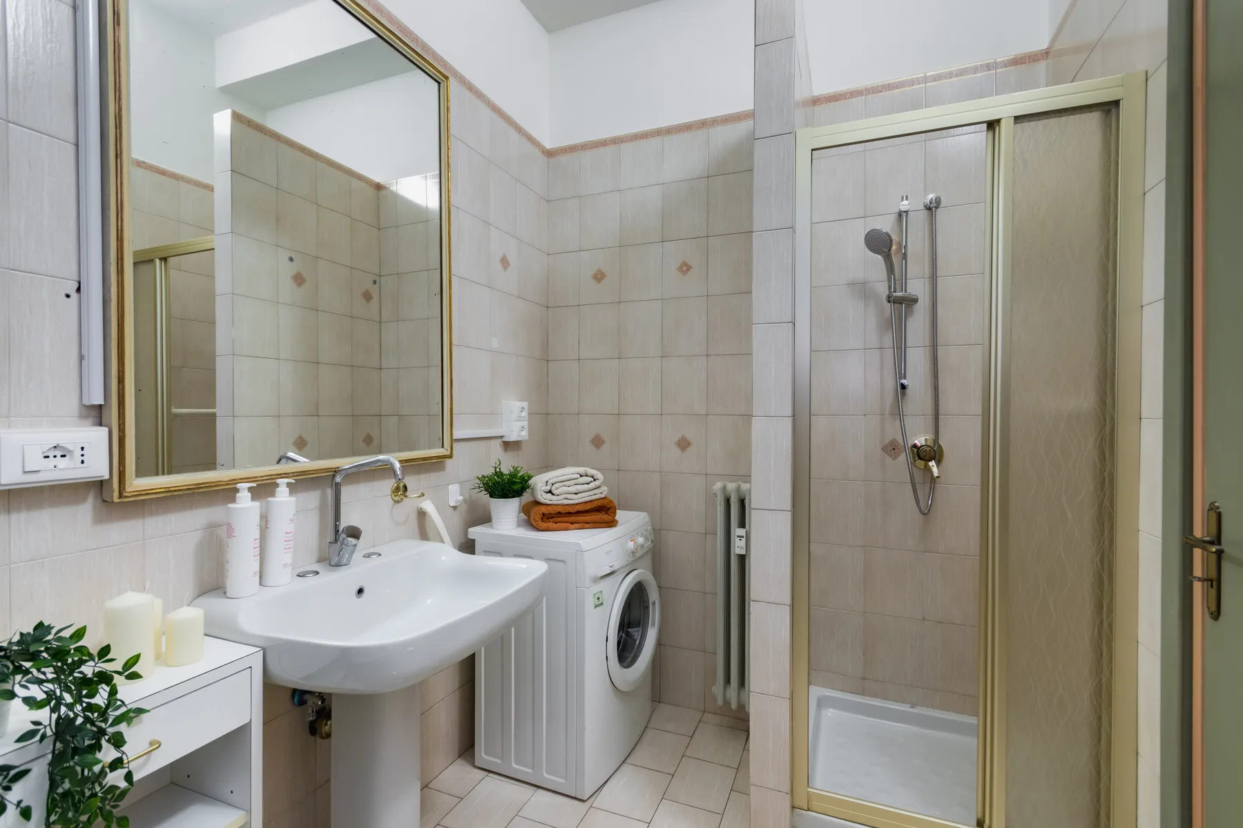 Un baño alicatado con lavabo, espejo, lavadora y ducha.