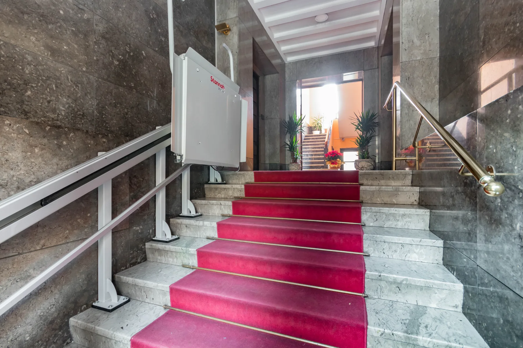 Una escalera de mármol con una alfombra roja conduce a un rellano iluminado.
