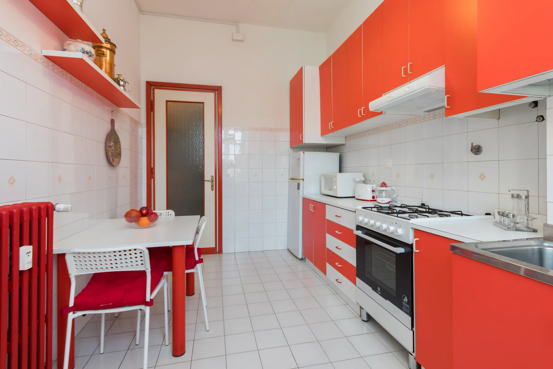Una cocina luminosa con armarios rojos, una estufa y una pequeña mesa de comedor.