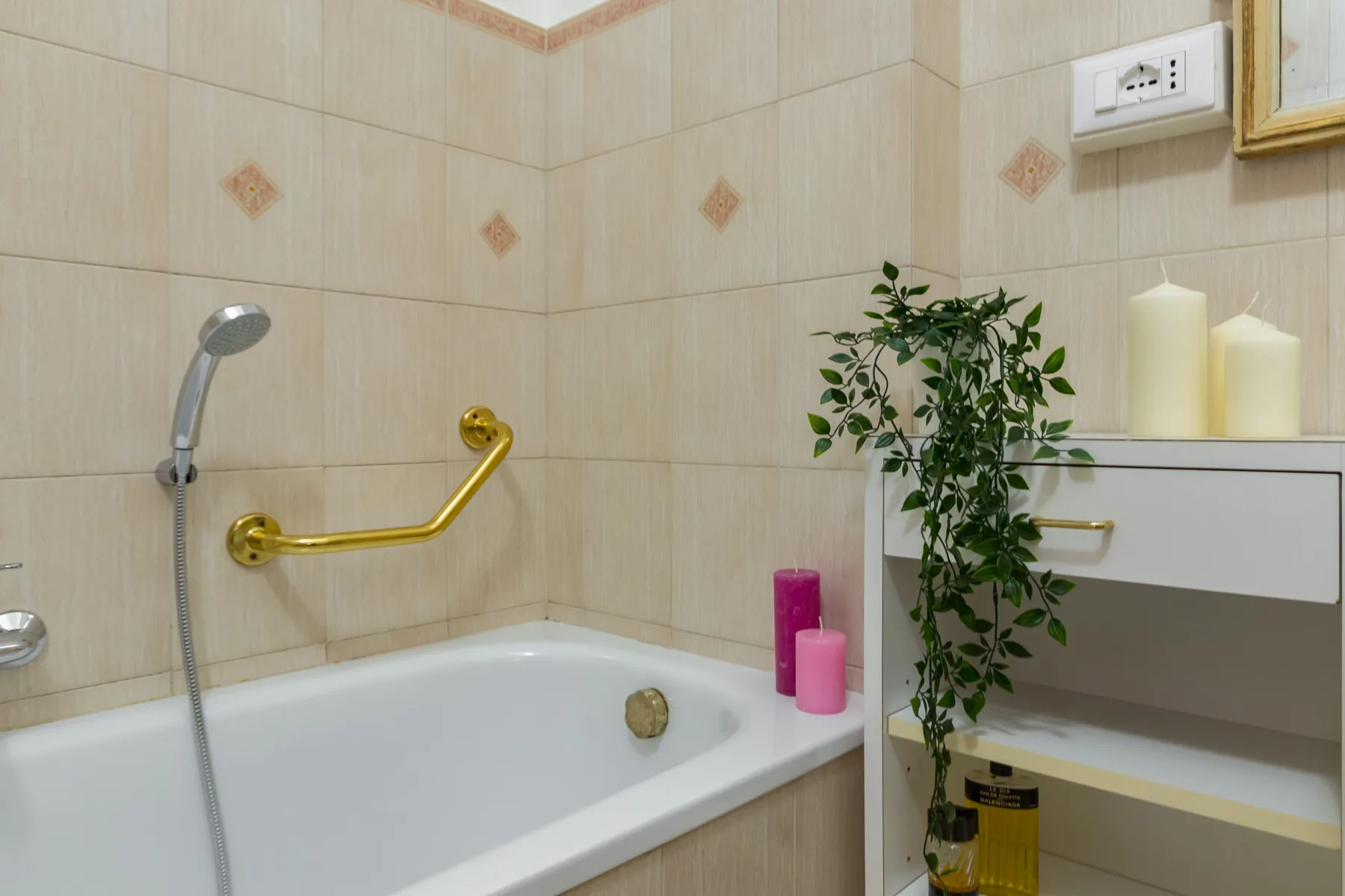 Un baño alicatado con bañera, ducha de mano y estantería.