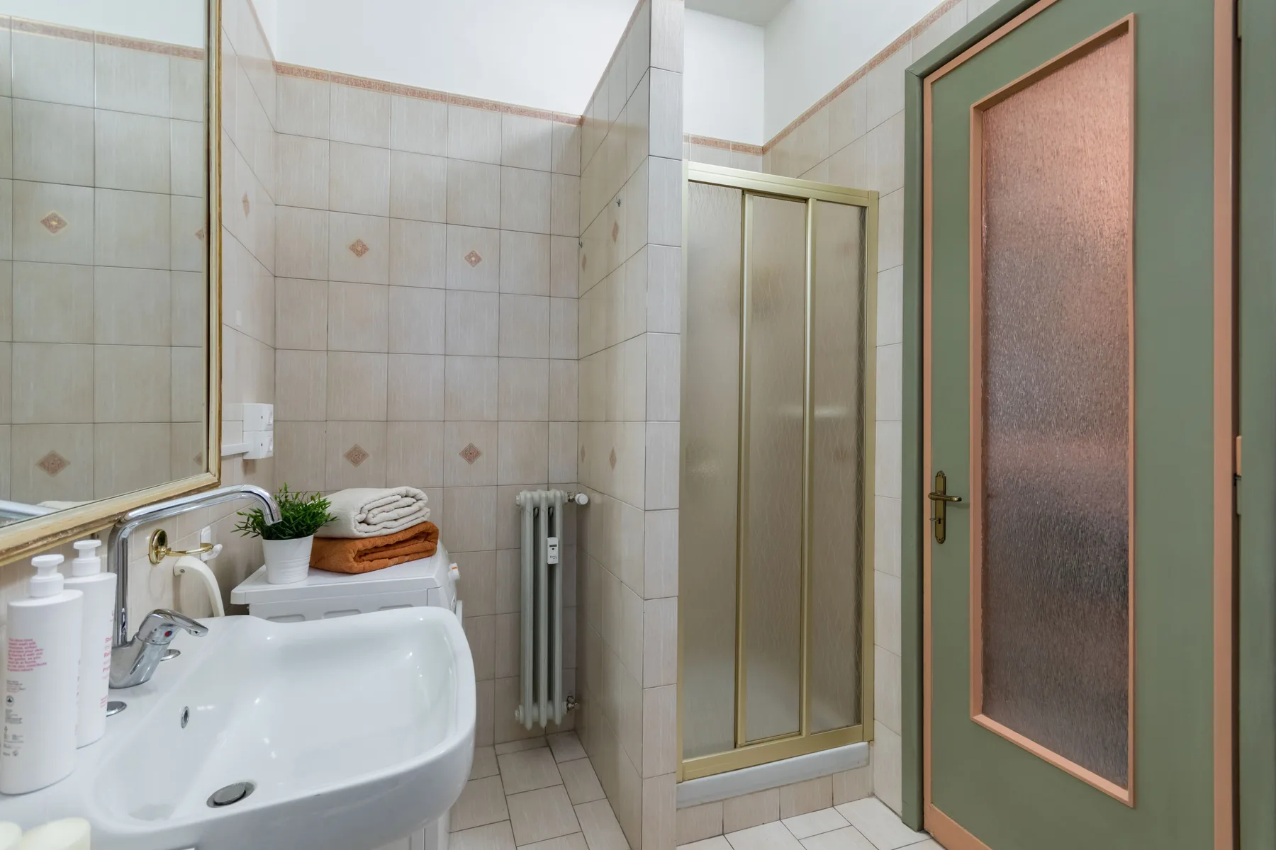 Un baño alicatado con lavabo, radiador y cabina de ducha.