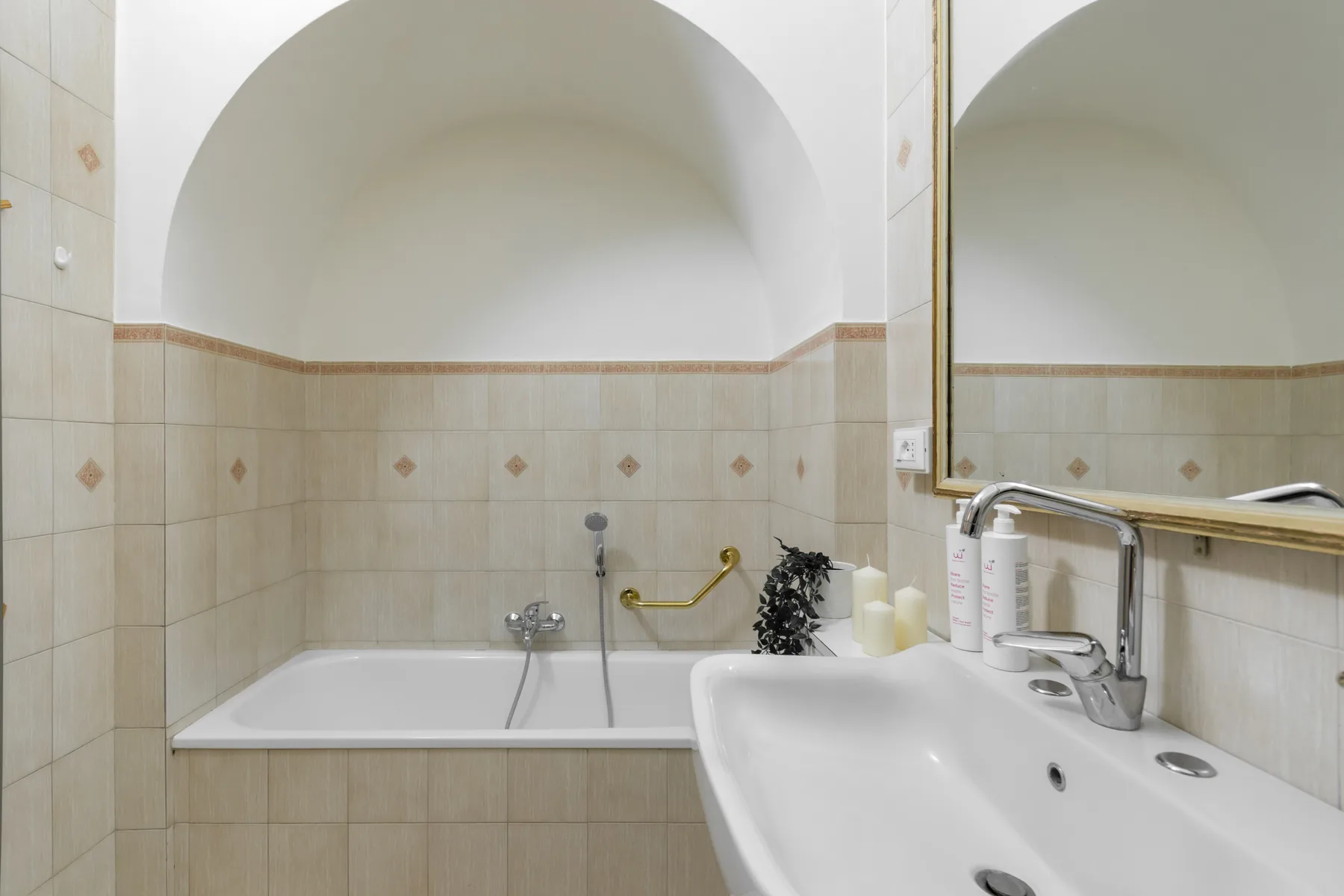 Un baño con azulejos, bañera y lavabo bajo un espejo grande.