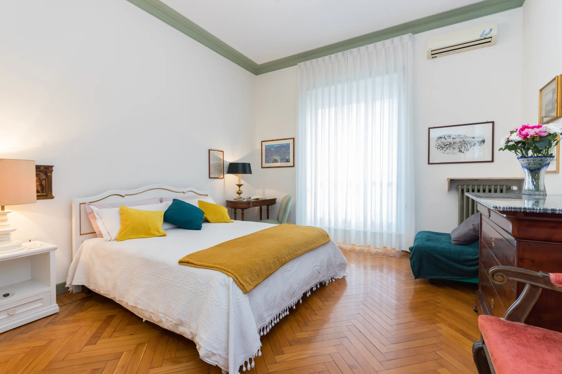 Un dormitorio con una cama grande, almohadas de colores y una ventana alta con cortinas.