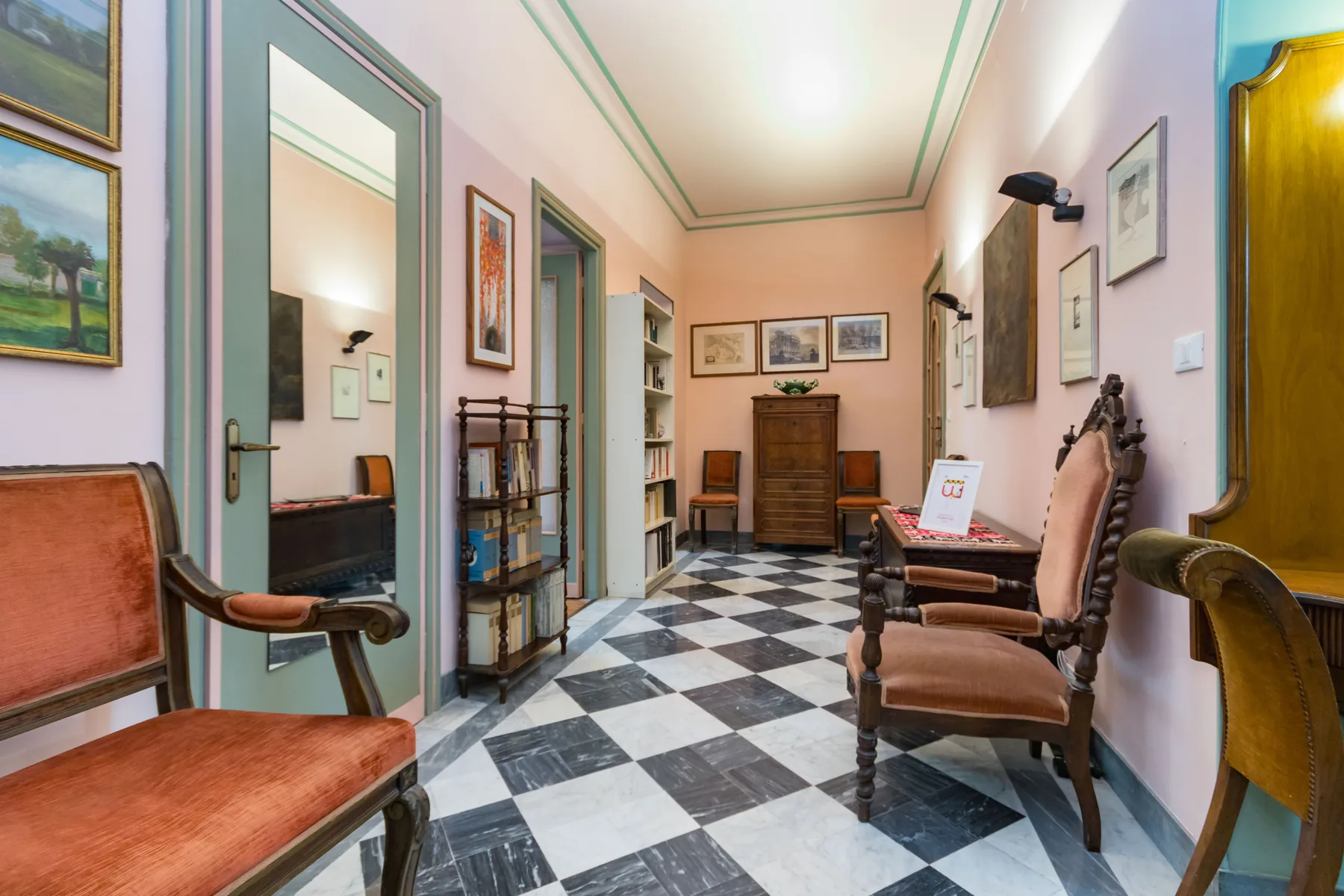 A furnished interior hallway has patterned tile flooring and seating along the walls.