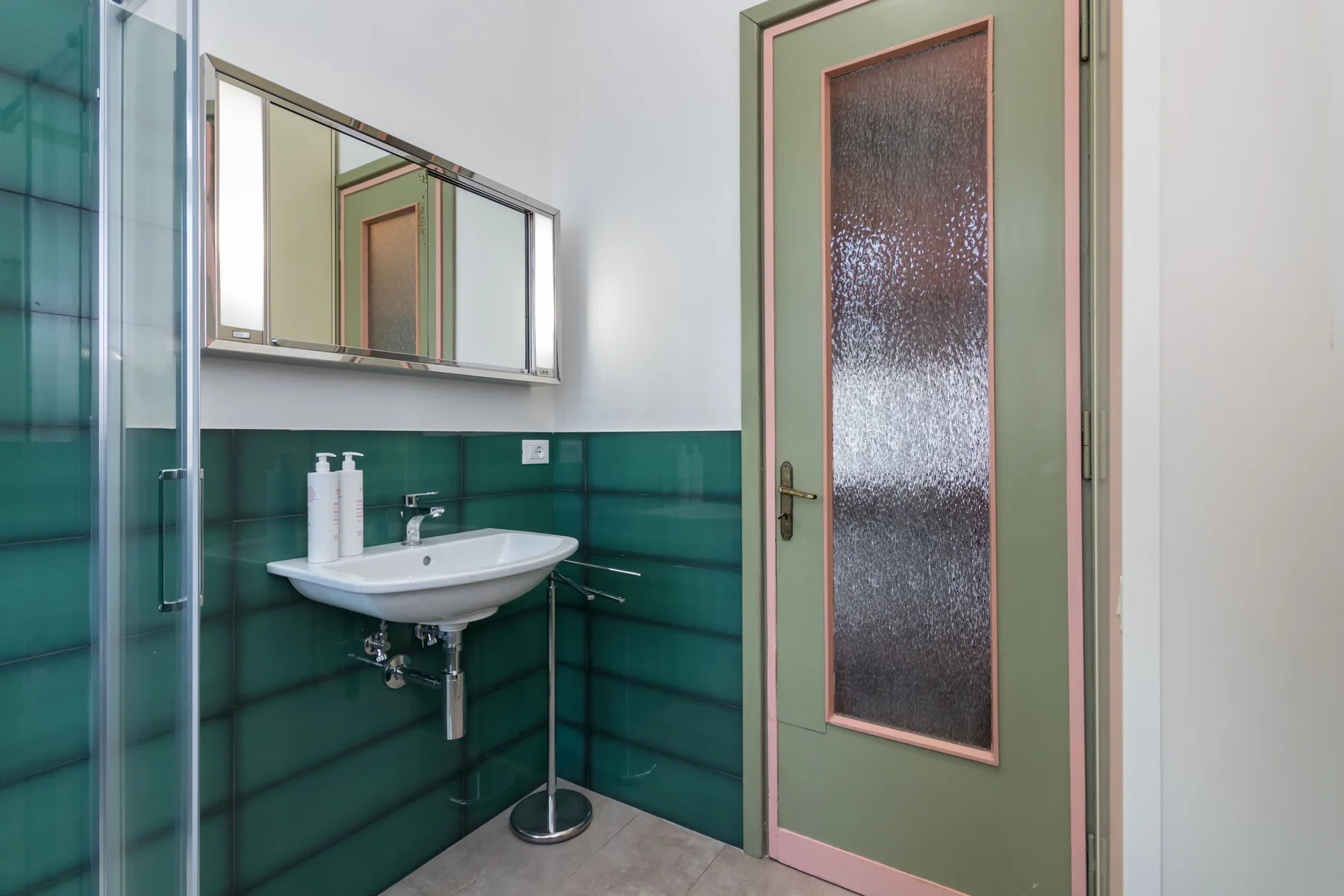 Un baño con lavabo de pared, espejo y ducha de vidrio.