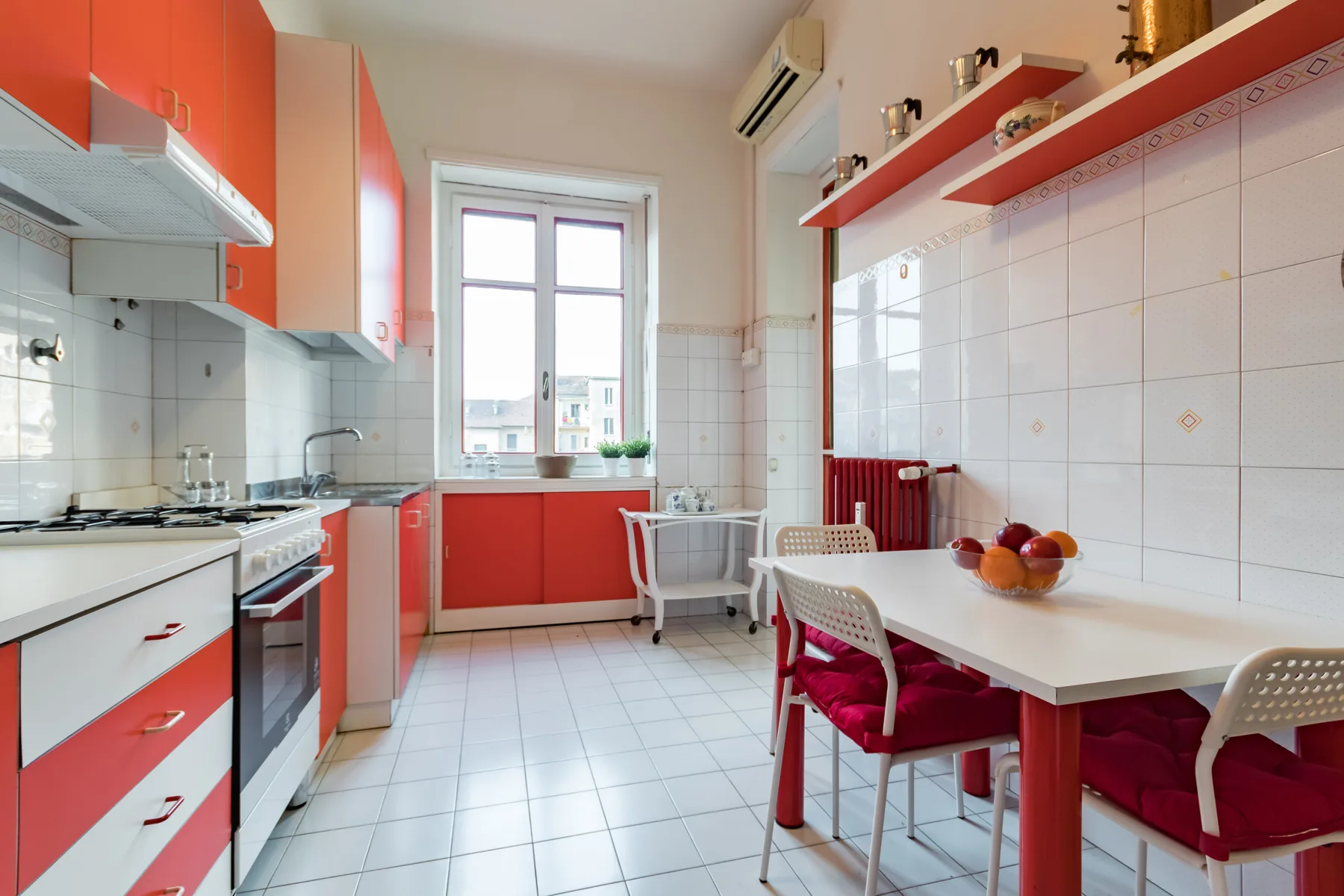 Una cocina luminosa con gabinetes rojos y una mesa junto a la ventana.