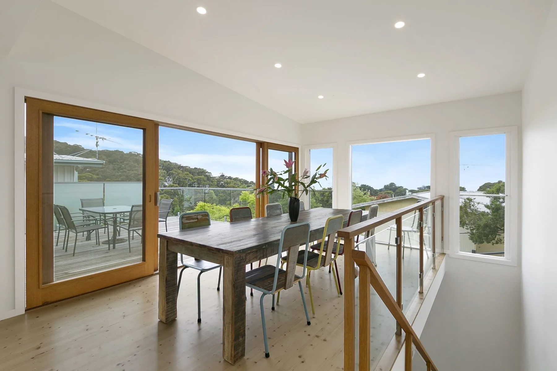 A dining area with a long table beside large windows and a balcony.