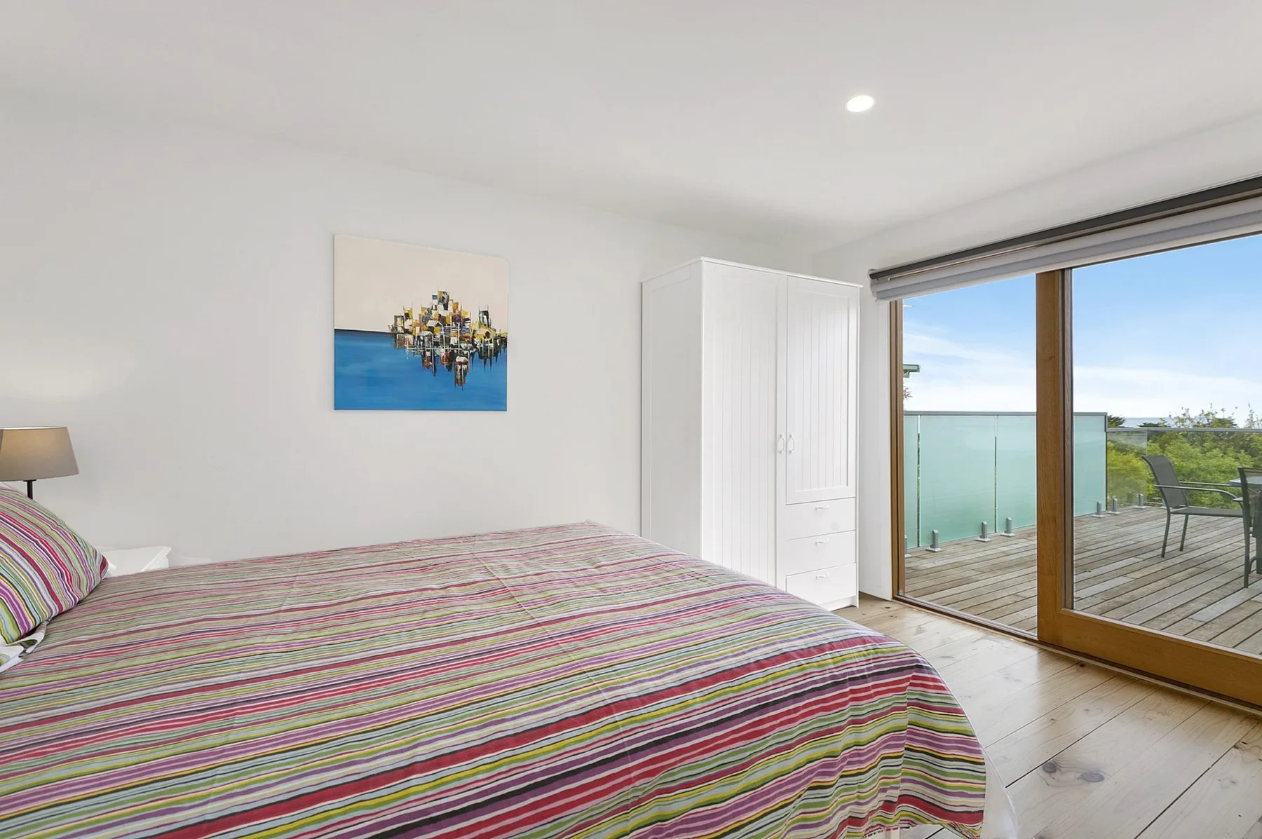 A bedroom with a striped bedspread and sliding glass doors opening onto a deck.