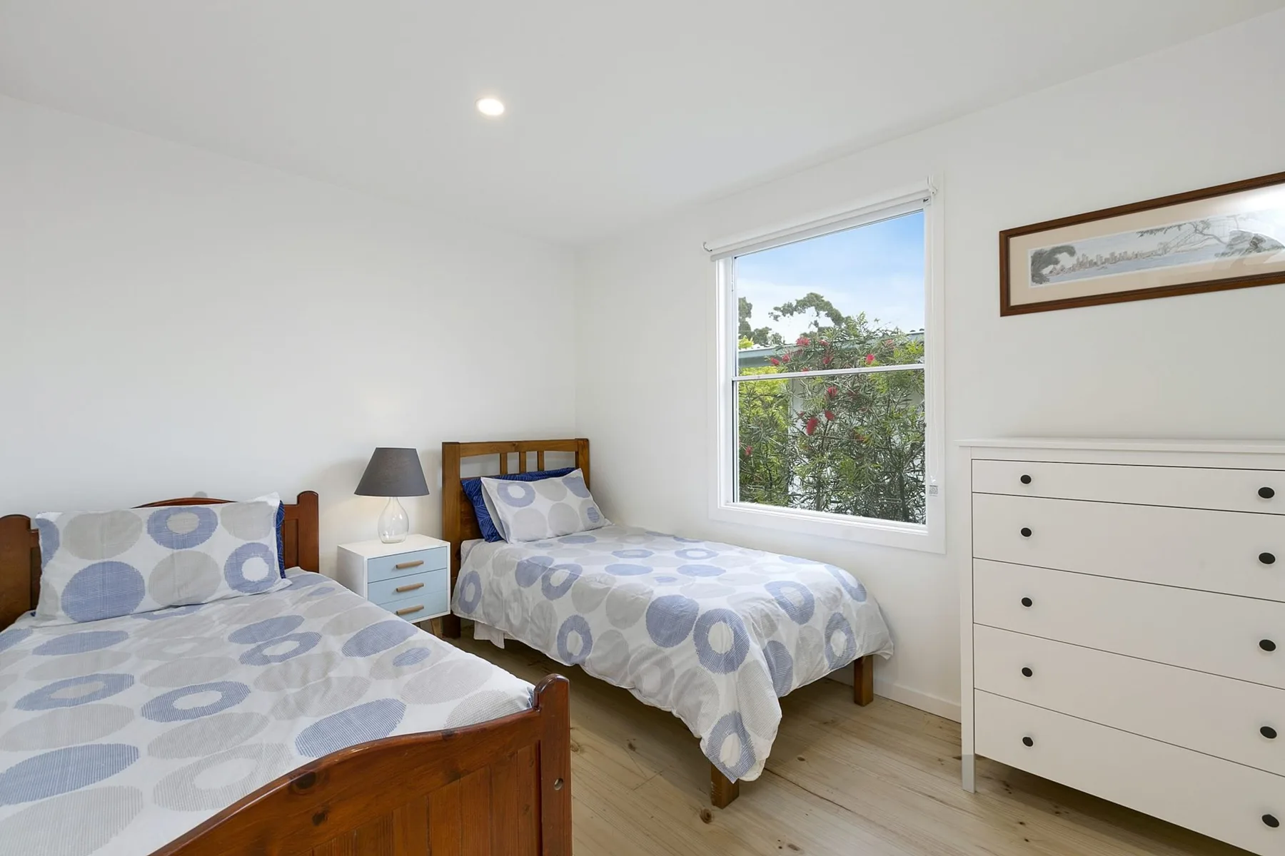 A bright bedroom with two beds and a window overlooking greenery.