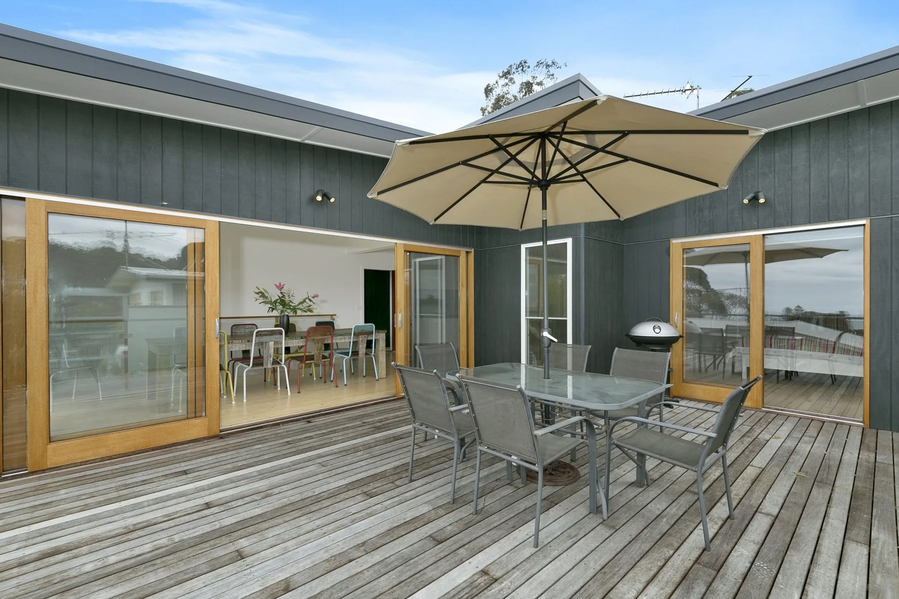 An outdoor deck with a dining table beneath a large umbrella.
