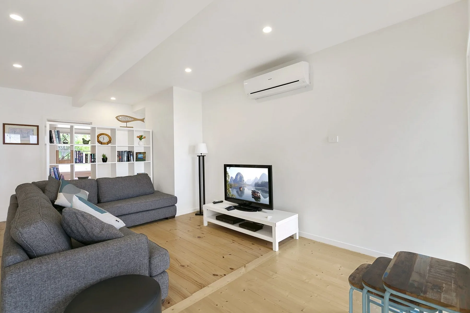 A bright living room with gray seating, a television, and open shelving.