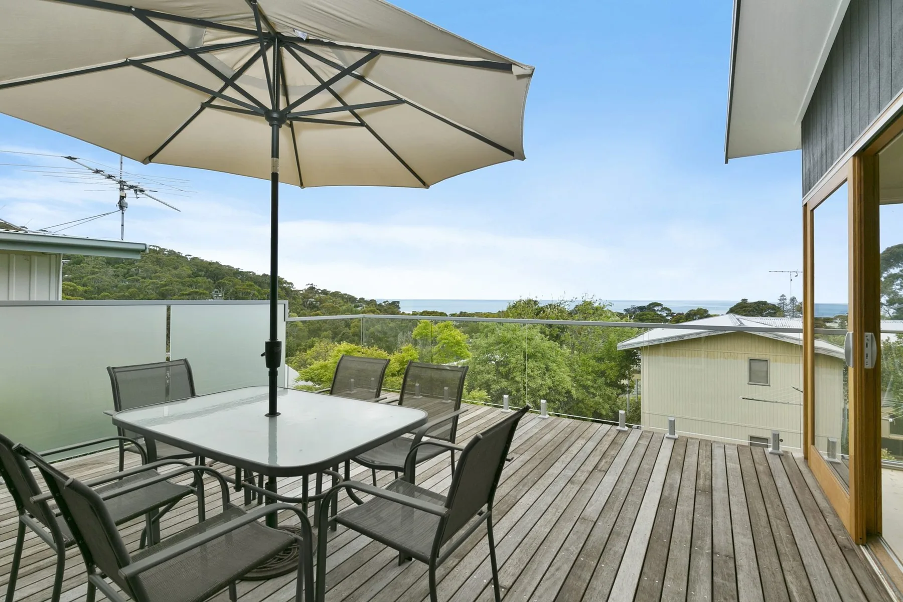 An outdoor deck with patio seating and a large umbrella overlooks greenery and distant water.