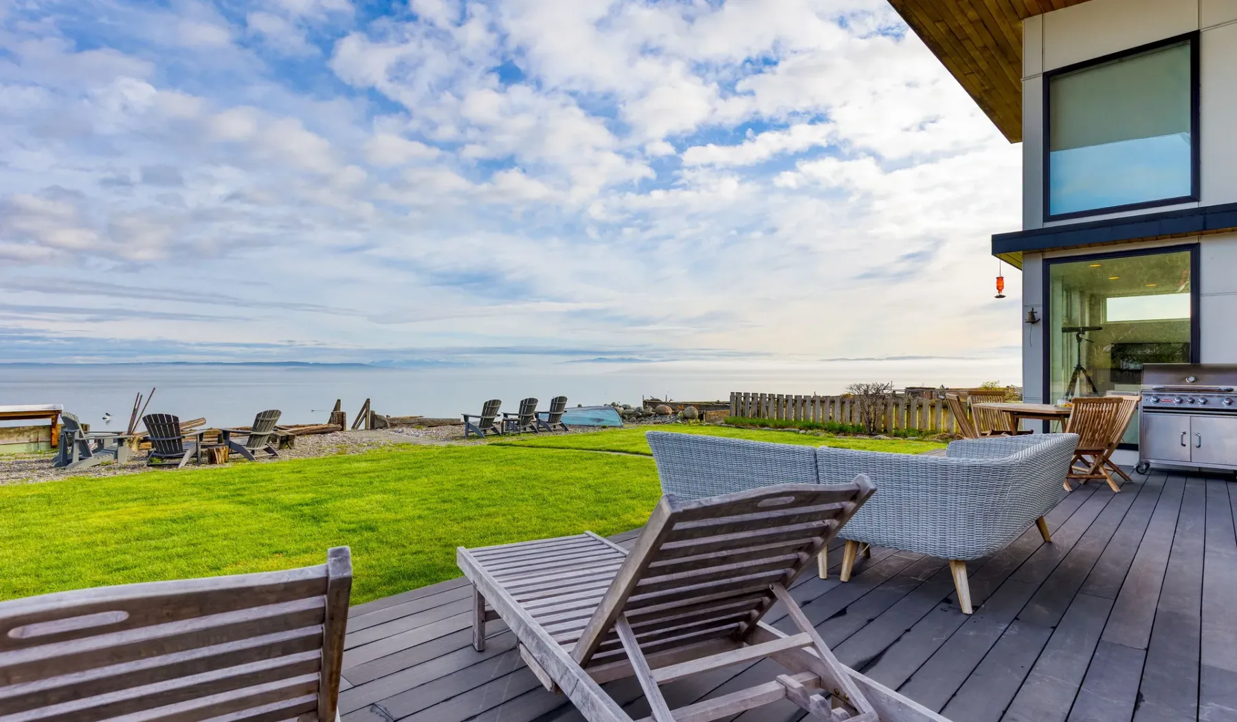 A seaside deck overlooks a grassy lawn and the water.