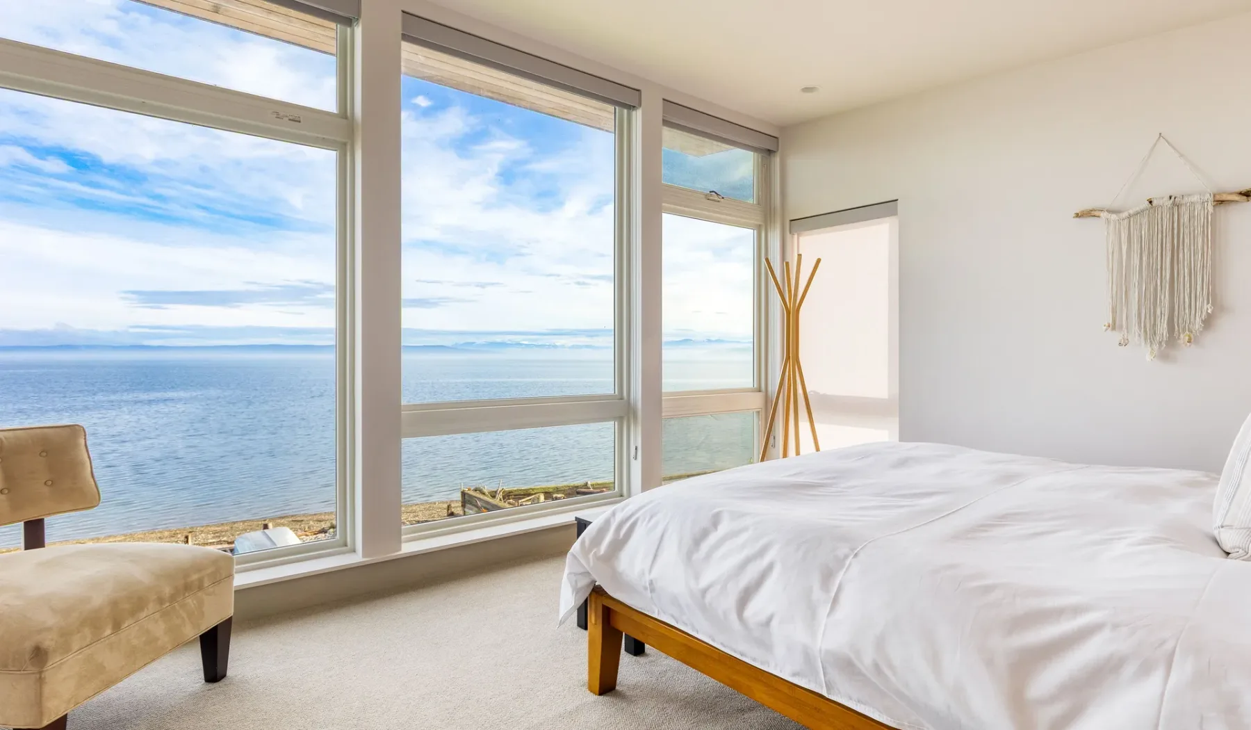 A bedroom with large windows overlooking the ocean and a bed in the foreground.