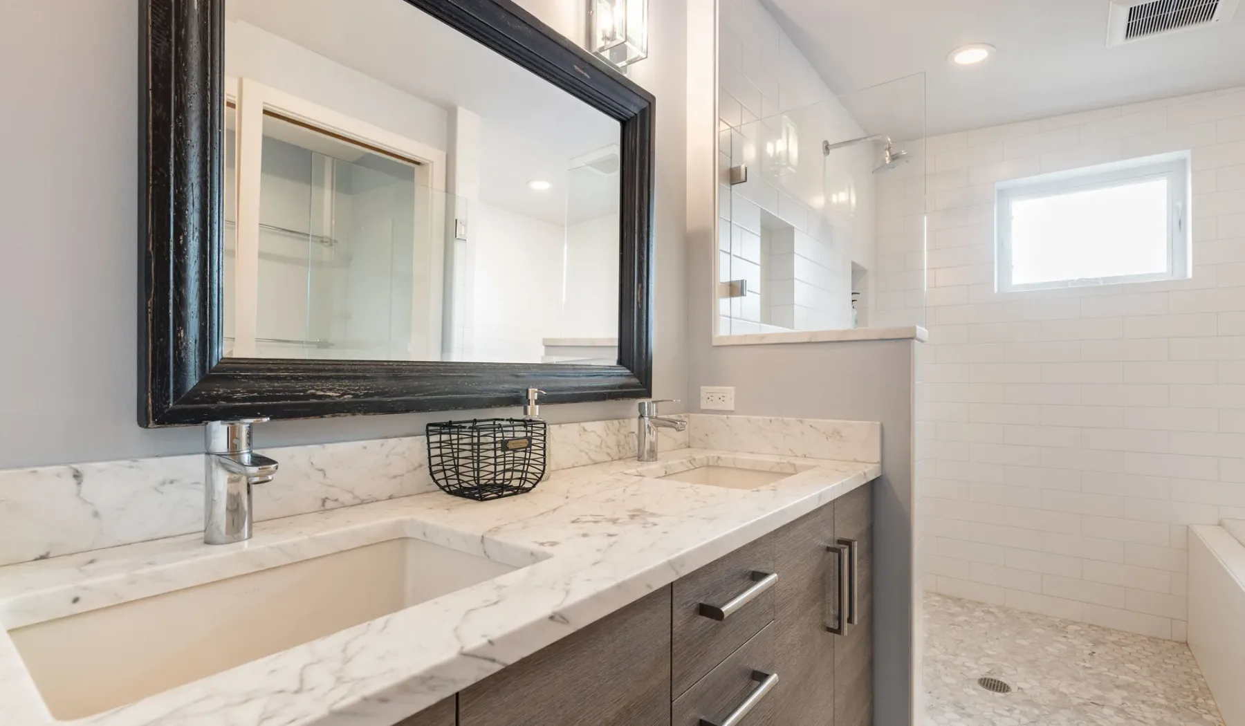A bright bathroom with a long vanity, large mirror, and walk-in shower.