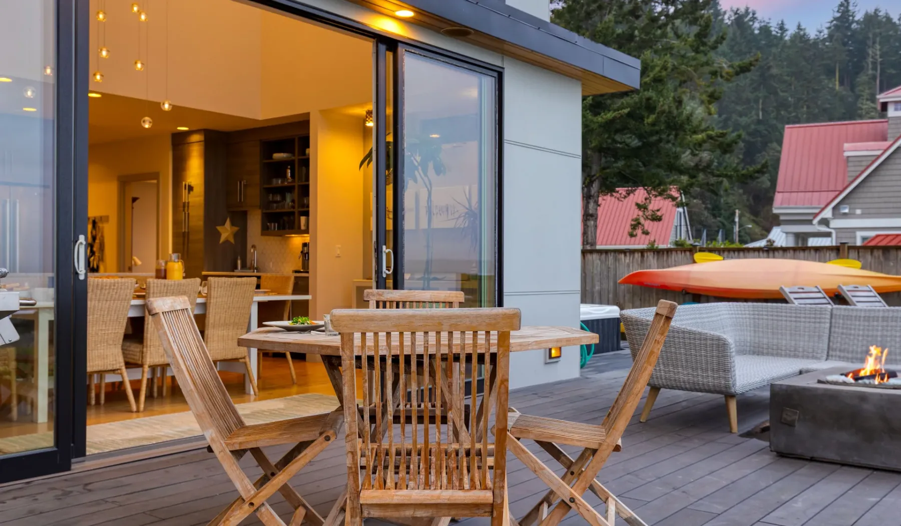 A furnished outdoor patio with wooden seating beside a warmly lit interior.