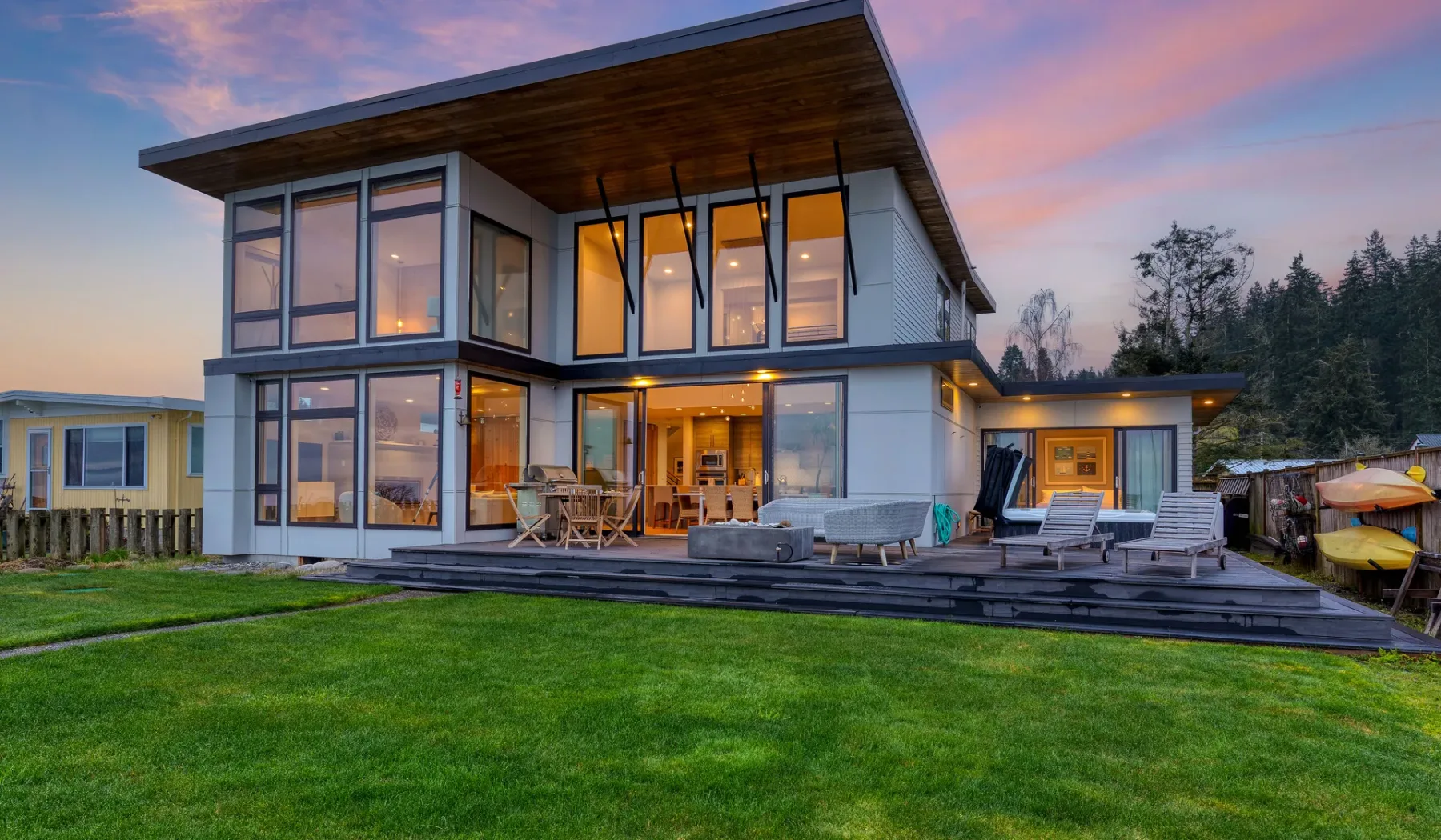 Modern two-story house with large windows and a lawn at dusk.