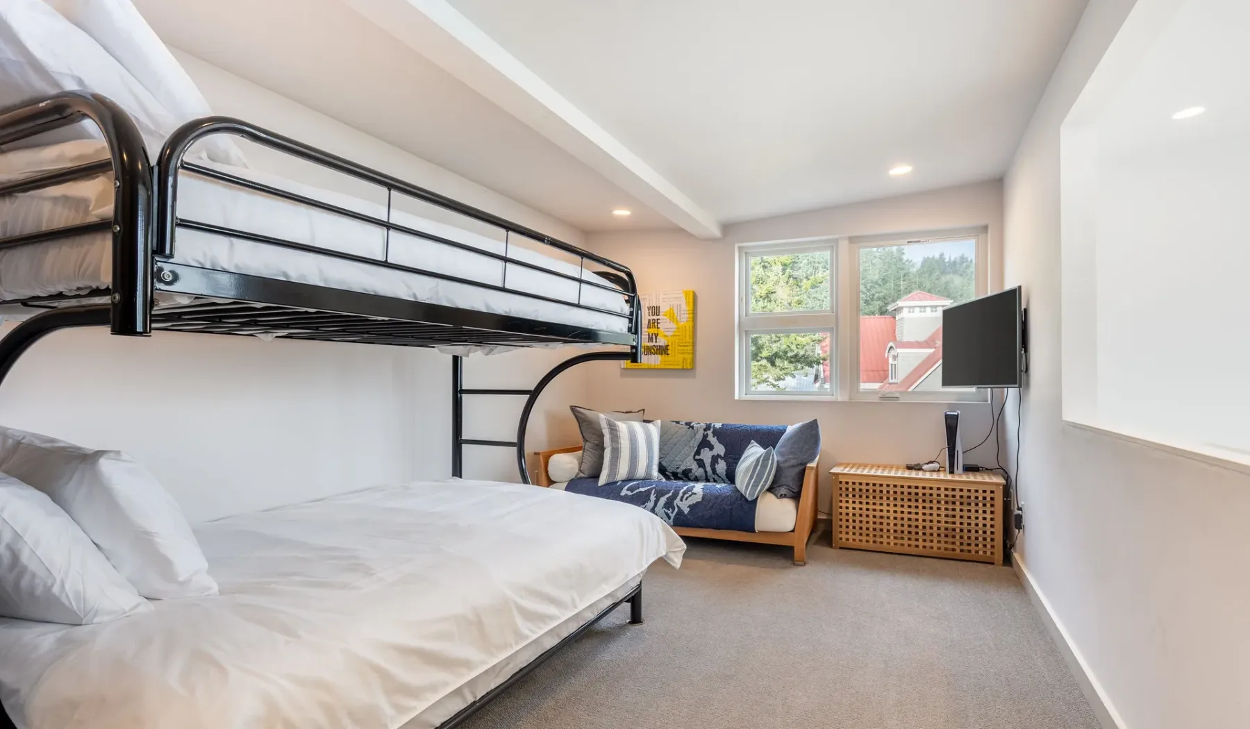 A bedroom with bunk beds, a small sofa, and a window overlooking greenery.