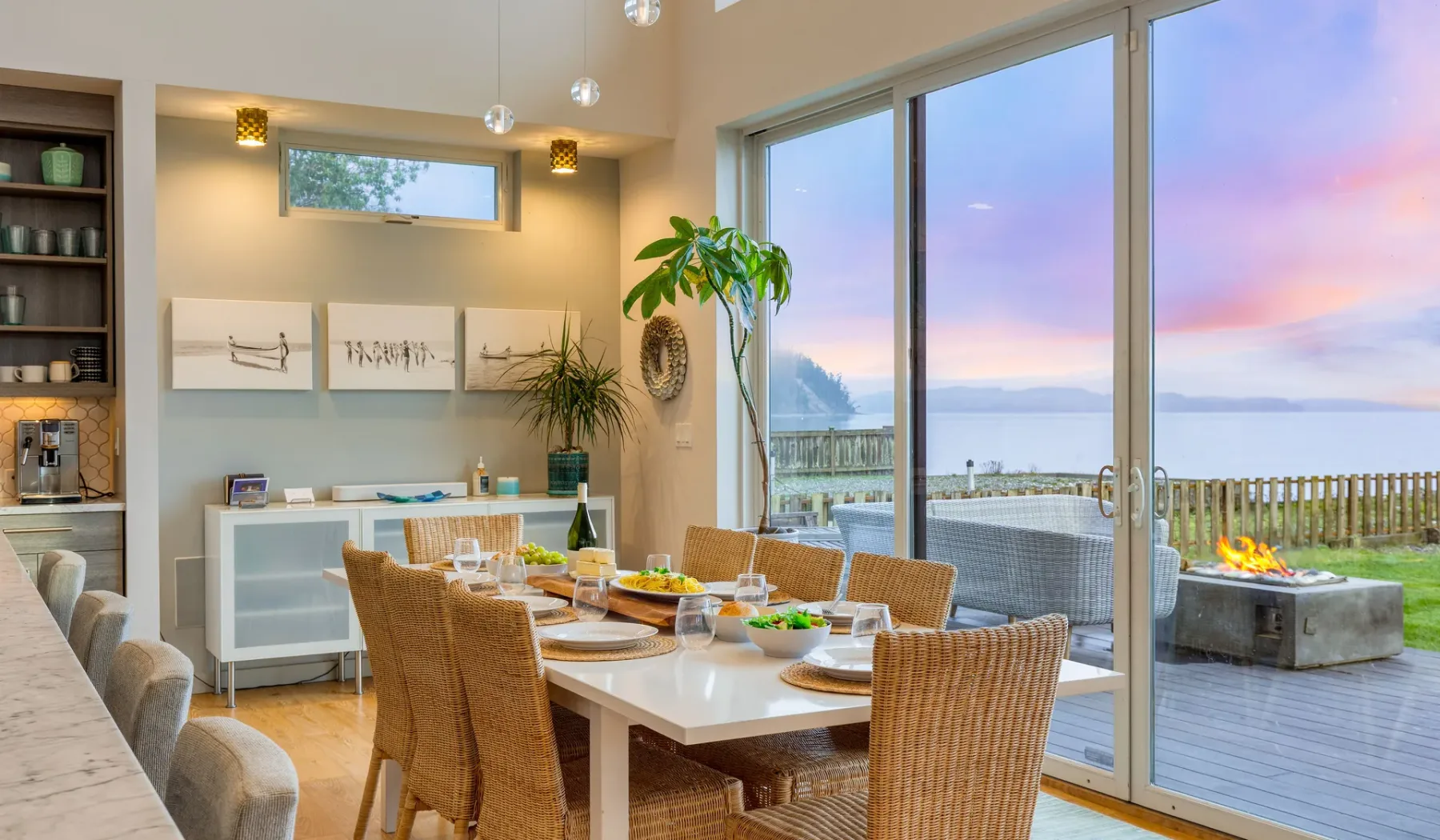 A dining area with wicker seating beside large windows overlooking the water.