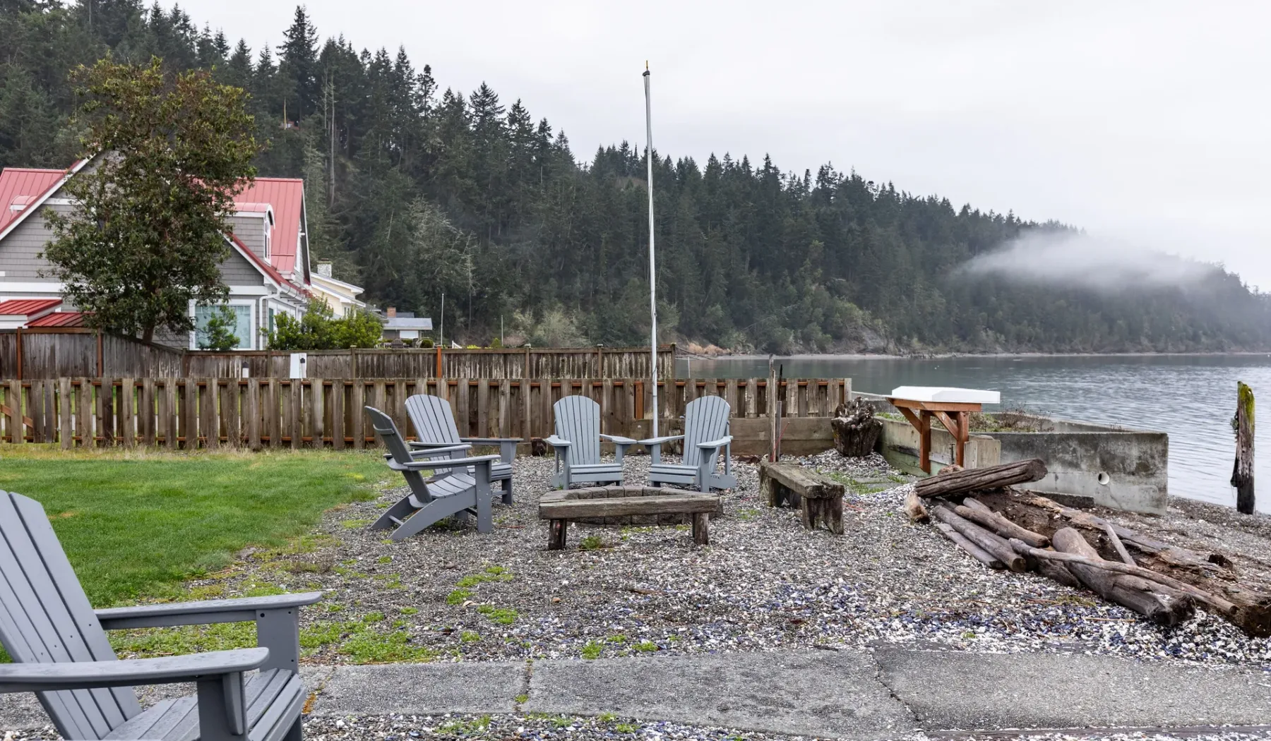 A lakeside seating area with chairs, a fire pit, and driftwood along the shore.