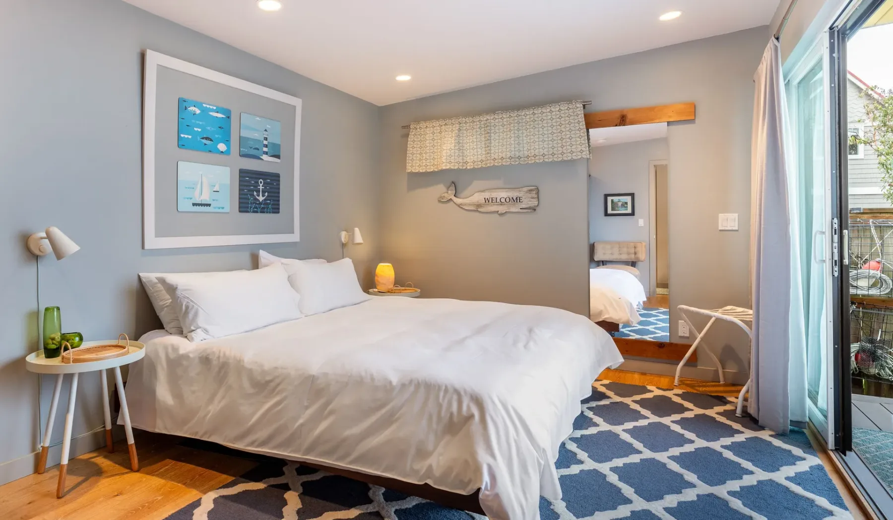 A bright bedroom with a neatly made bed and a blue patterned rug.
