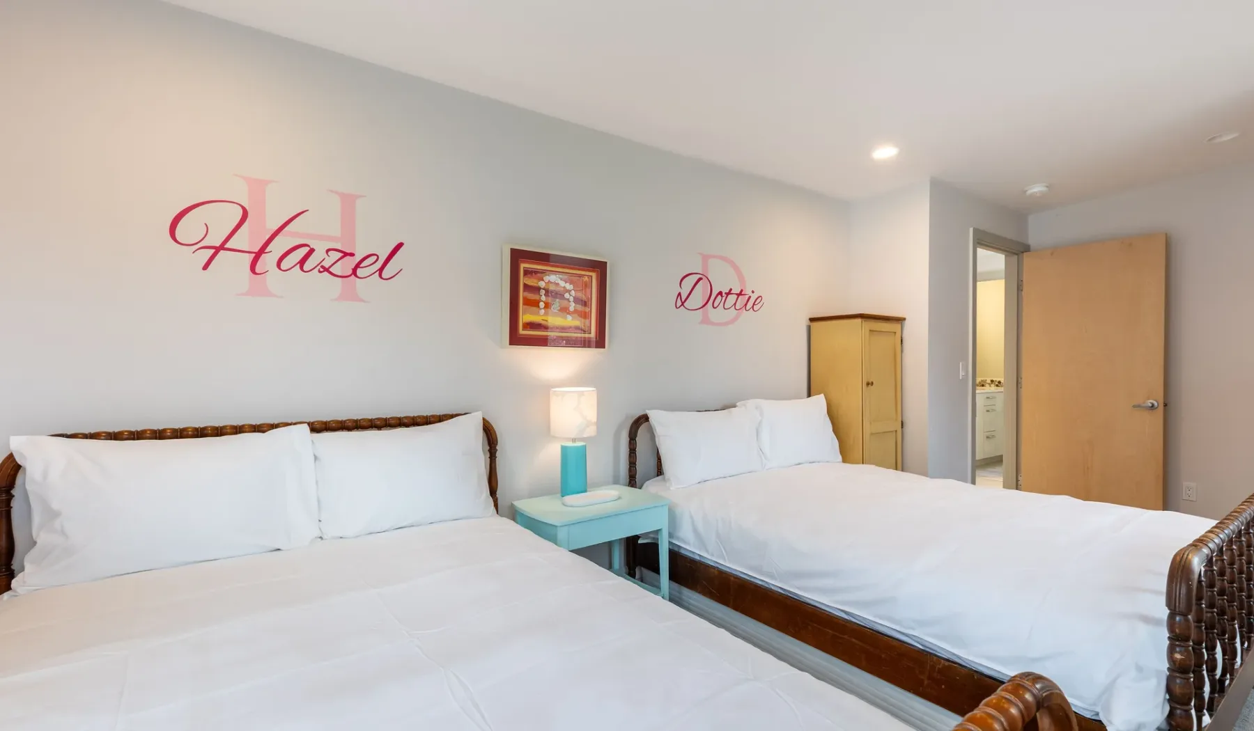 A bedroom with two beds, bedside tables, and decorative wall lettering.