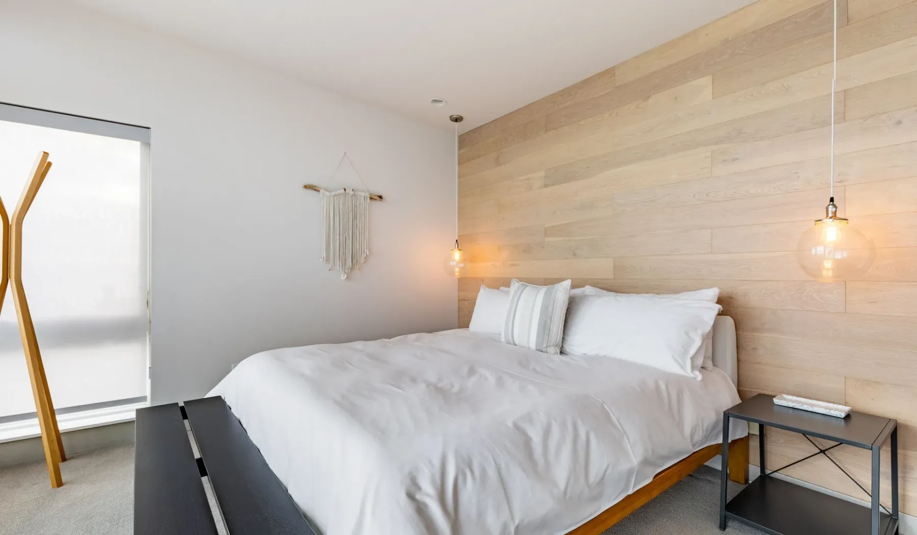 A bedroom with a neatly made bed and a light wood accent wall.