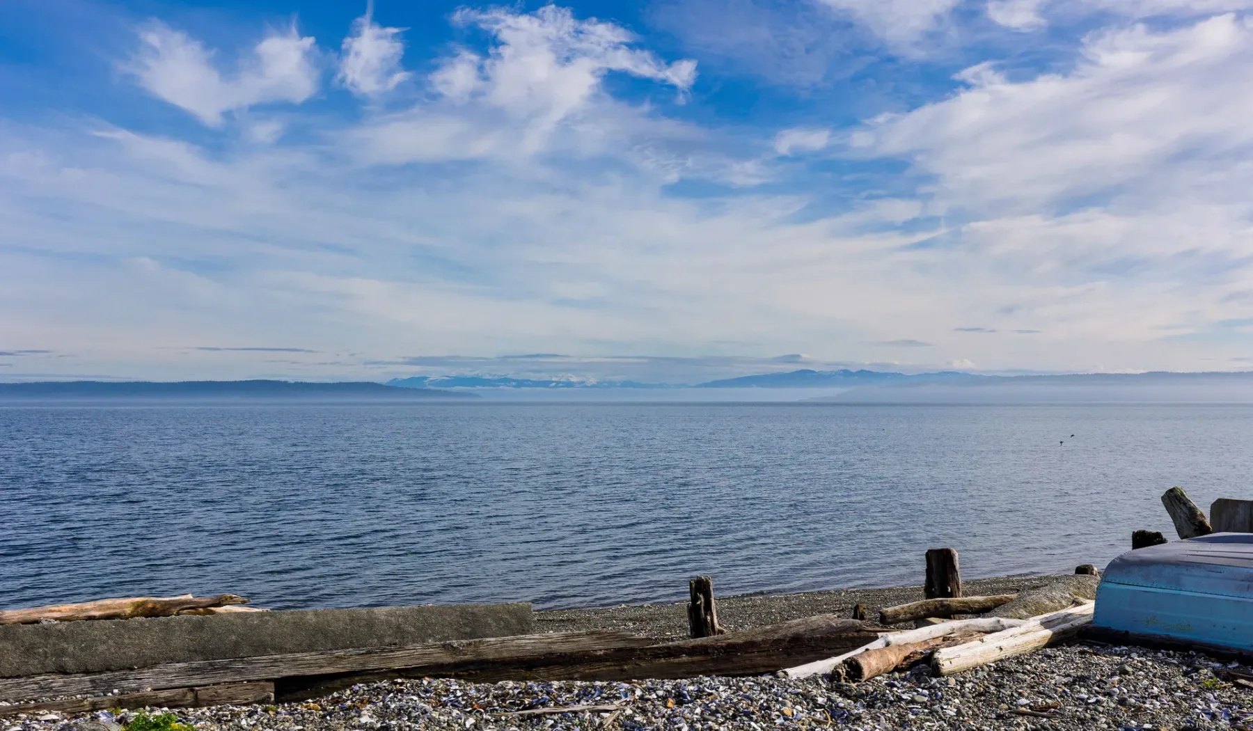A calm body of water stretches beneath a partly cloudy sky, with a rocky shoreline in the foreground.