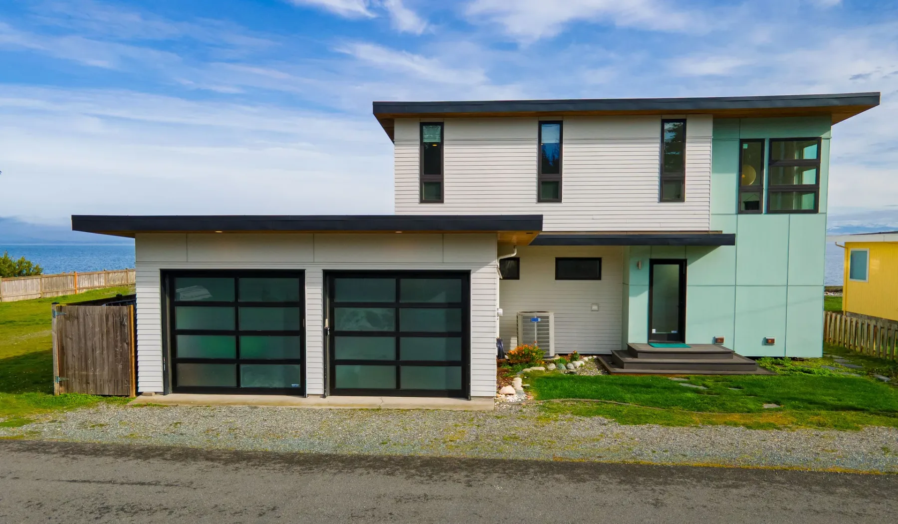 A modern two-story house with dark-framed windows stands beside a gravel drive.