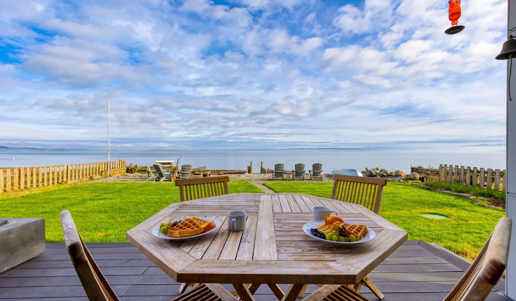 A patio dining table overlooks a grassy lawn and the ocean.