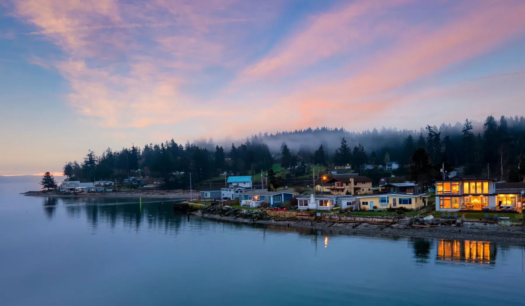 A waterfront settlement sits beside calm water beneath a colorful evening sky.