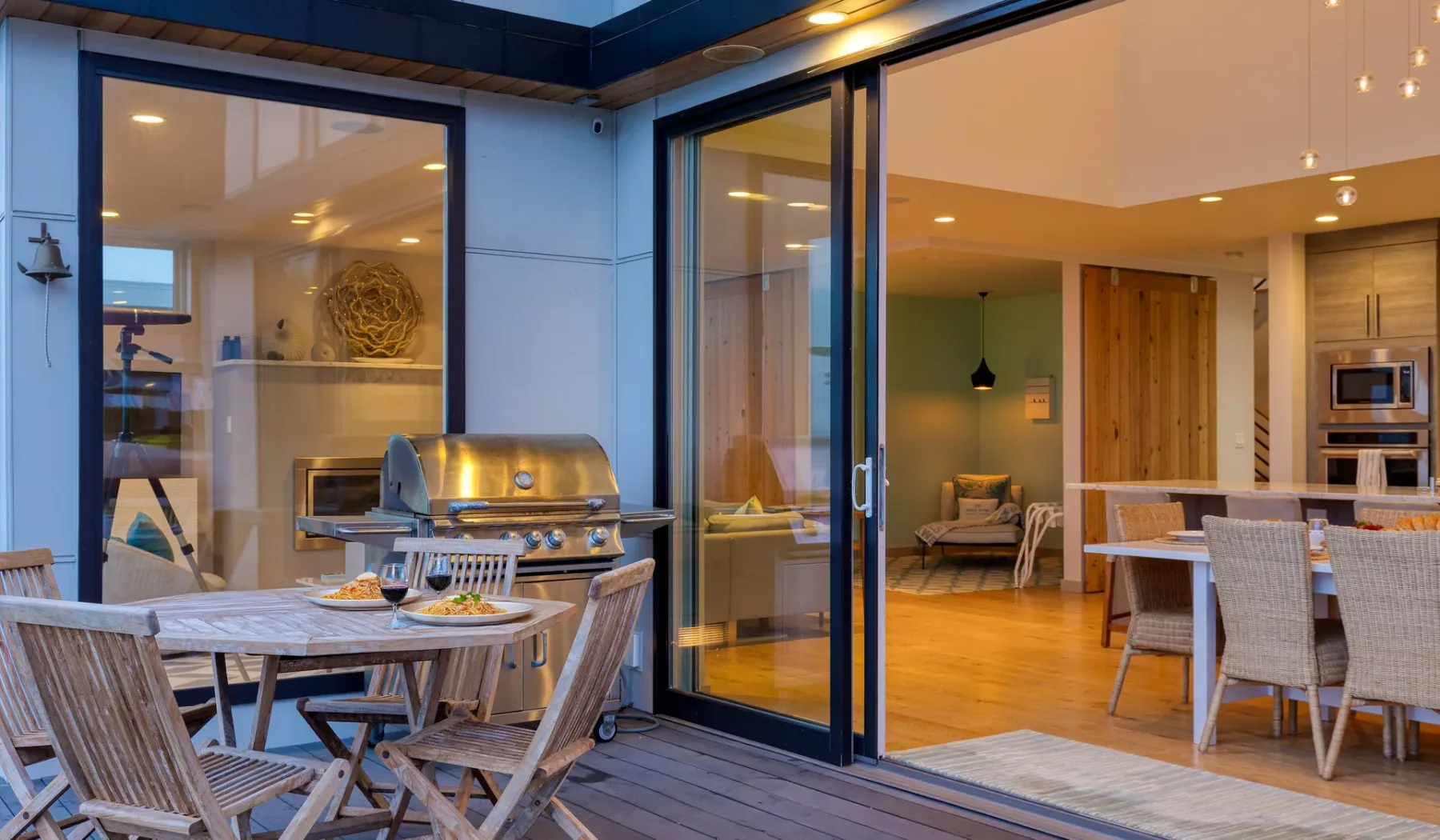 A dining patio with outdoor seating and a grill opens onto an indoor living area.
