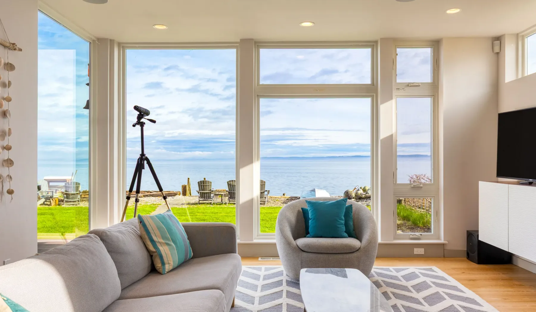 A bright living room with seating beside large windows overlooking the ocean.