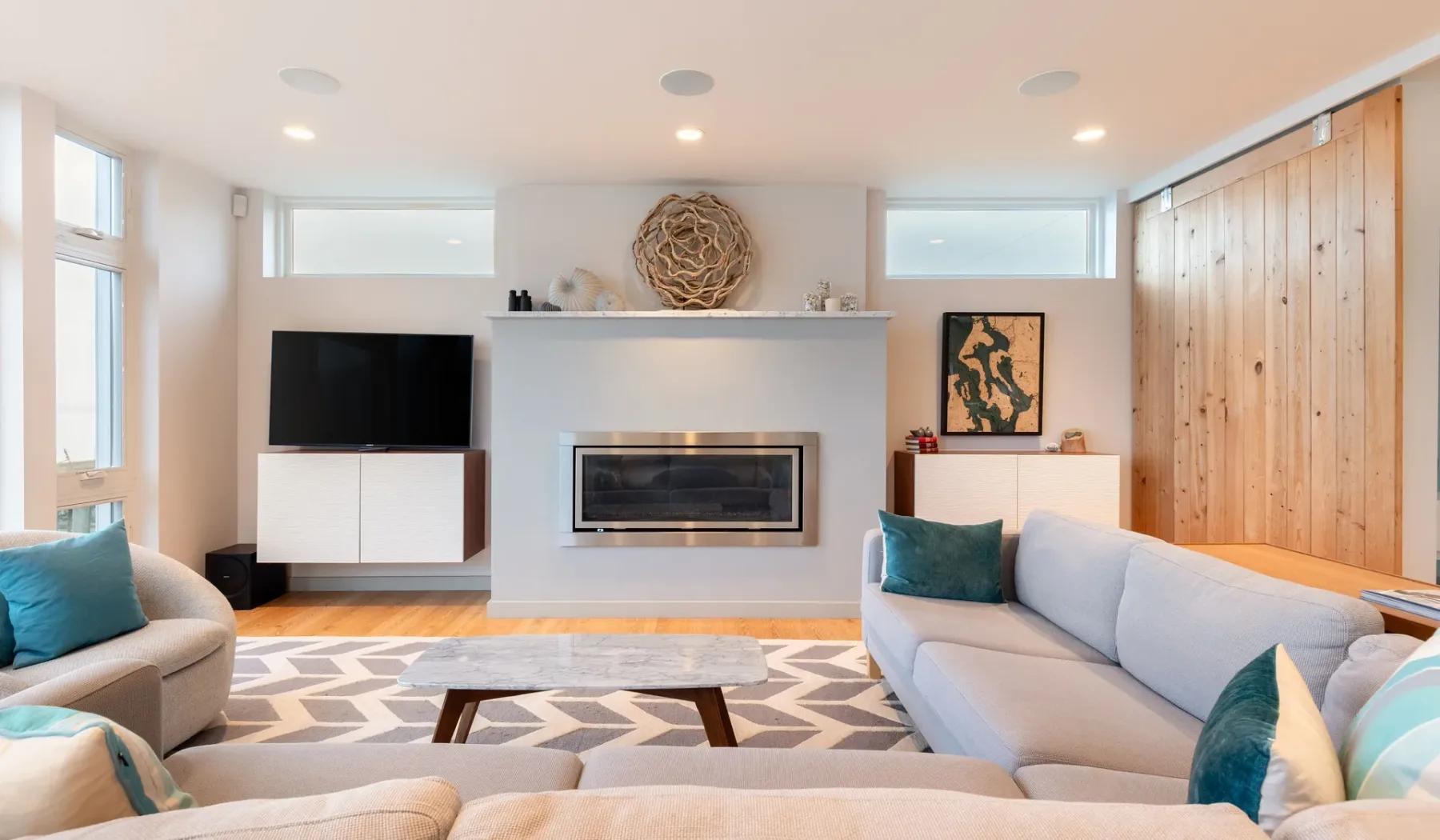 A bright living room with seating around a fireplace and a patterned rug.