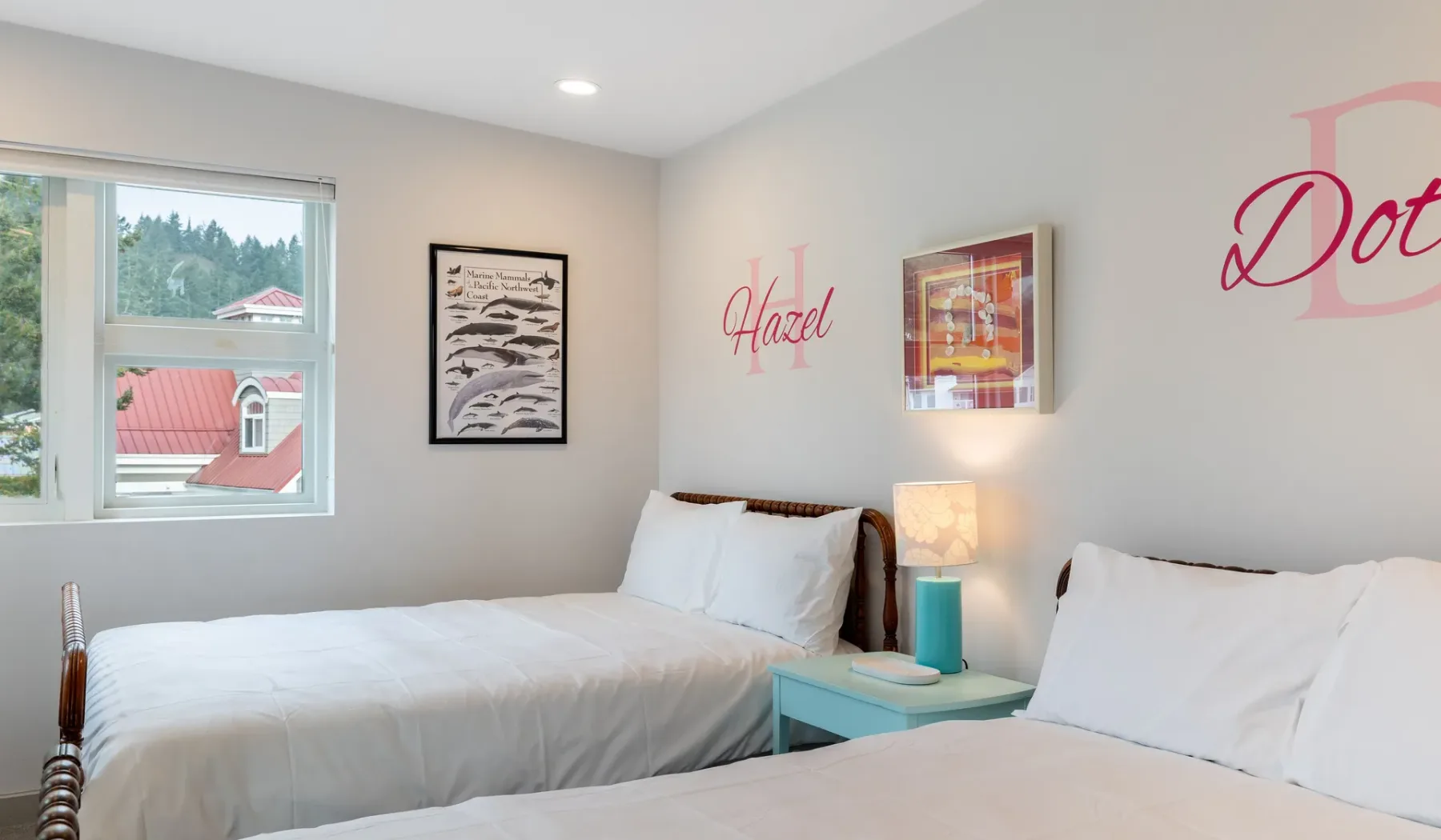 A bright bedroom with two beds, a window, and framed wall art.