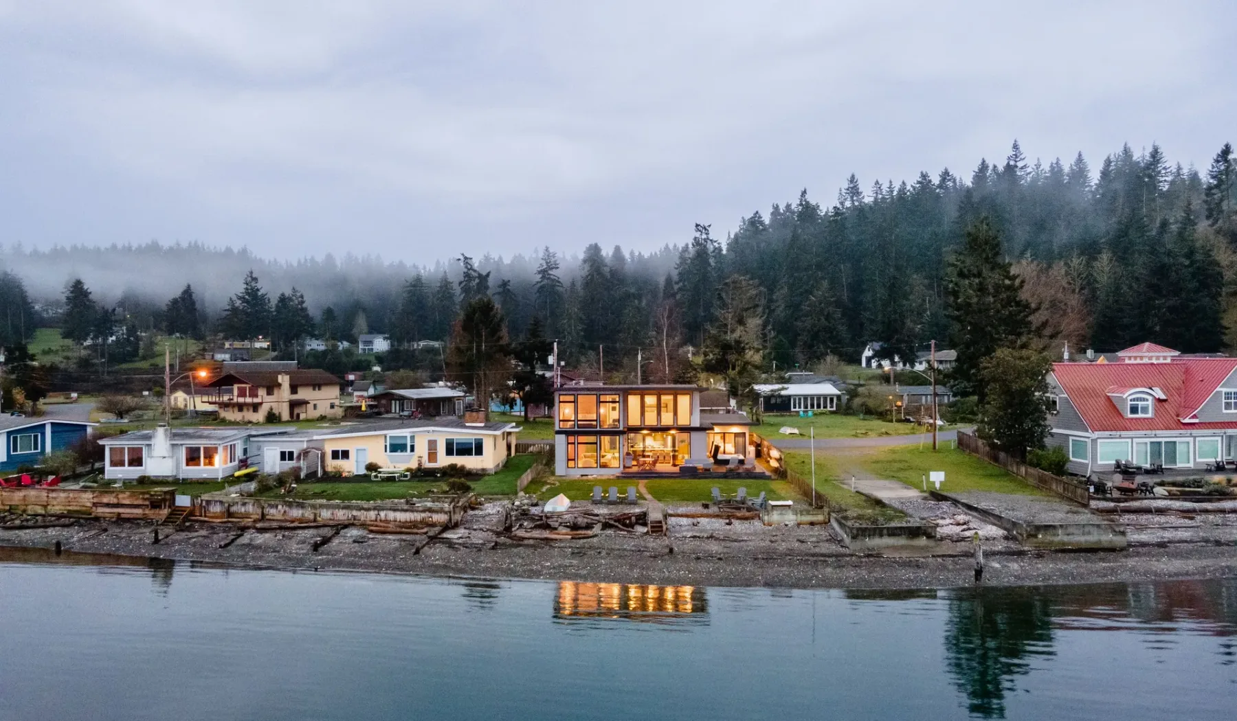 A waterfront residential area sits beneath a misty, forested hillside.