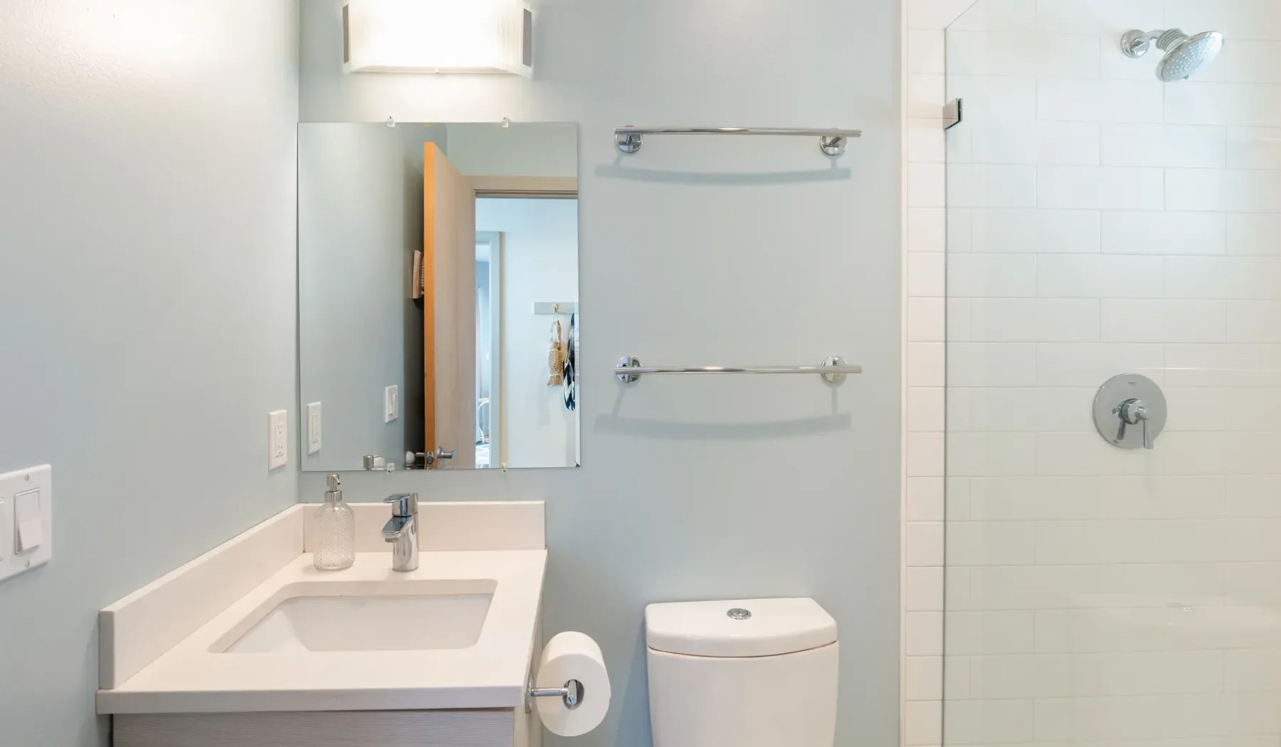 A bright bathroom with a sink, toilet, and tiled shower.